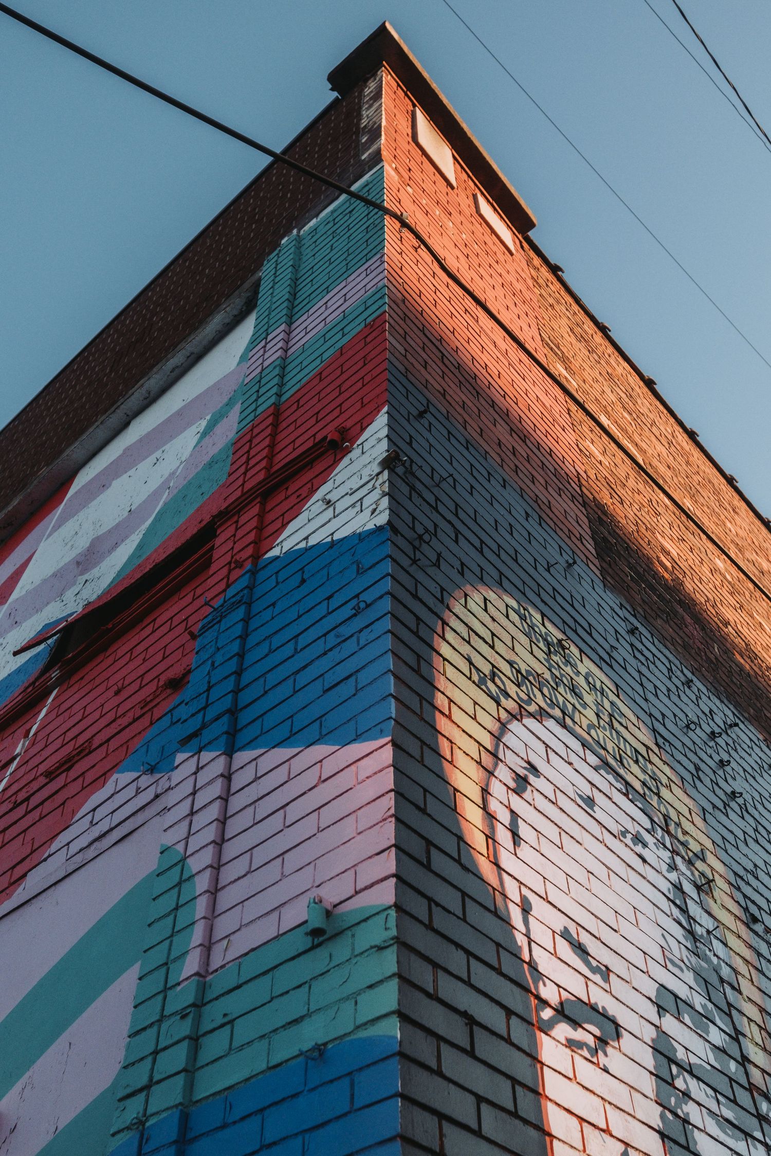 Colorful geometric mural painted on brick building facade against blue sky.