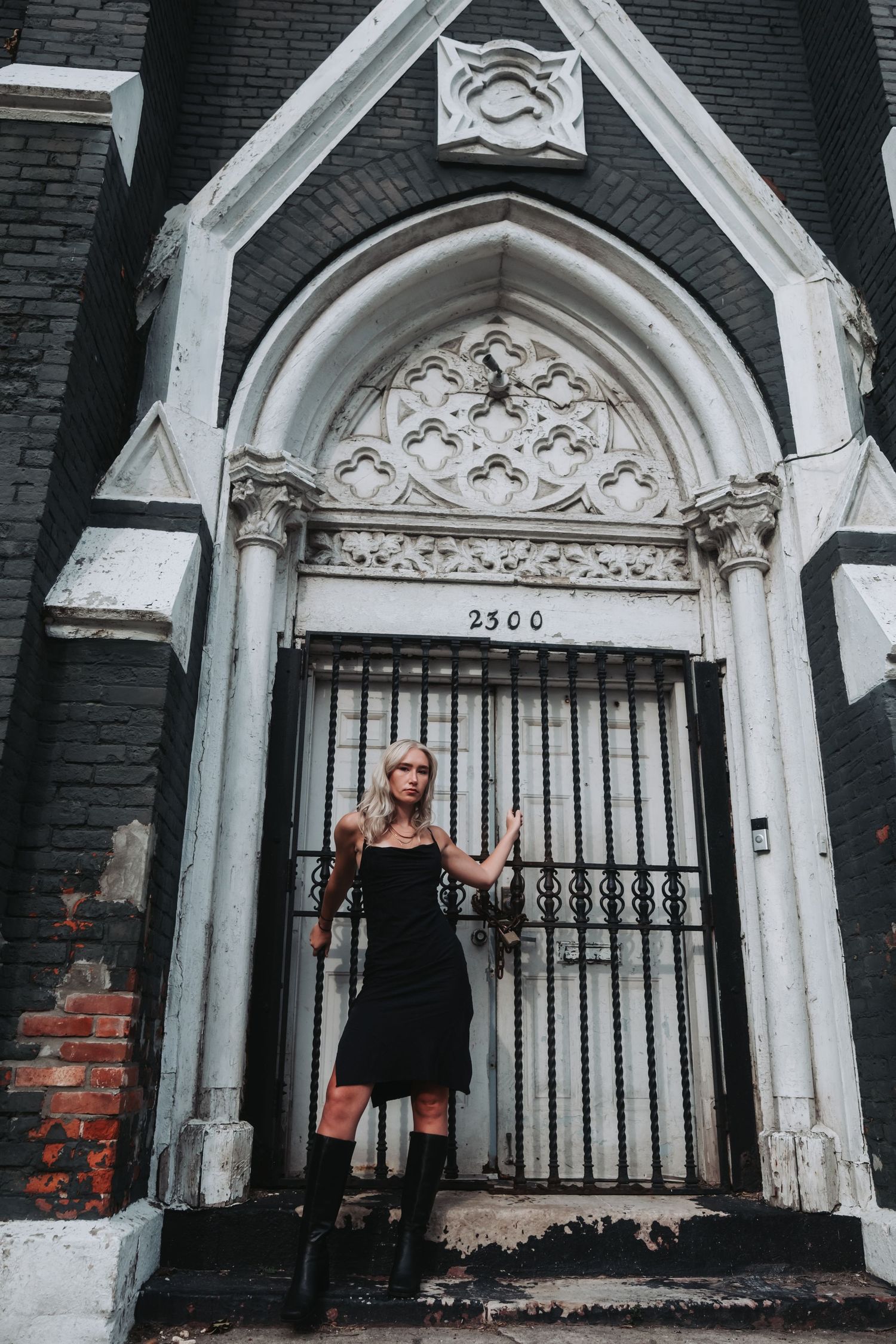 Blonde woman in black dress and boots posing before gothic church entrance at 2300.