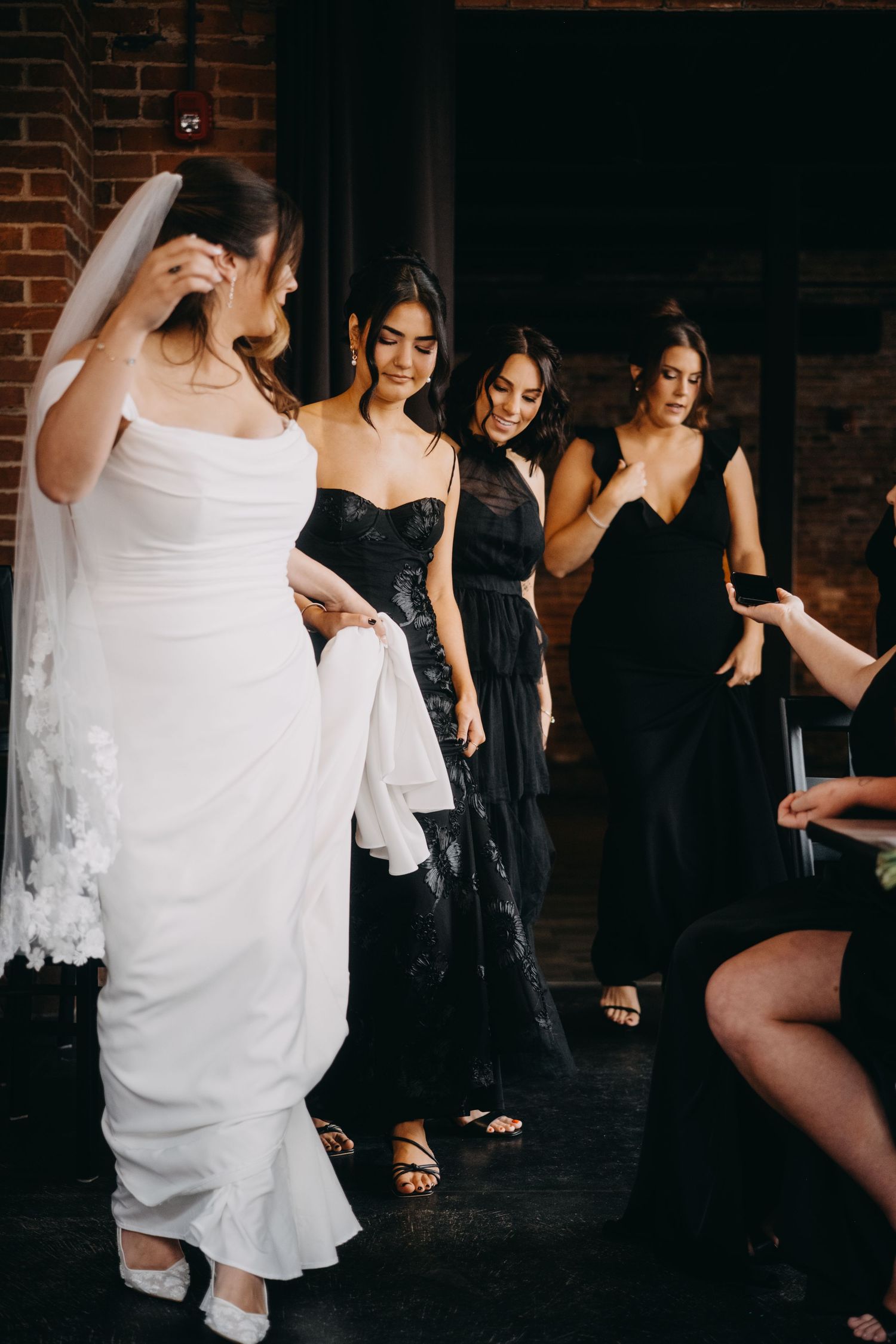Bride in white gown with veil walks alongside bridesmaids in black dresses at an elegant wedding reception.