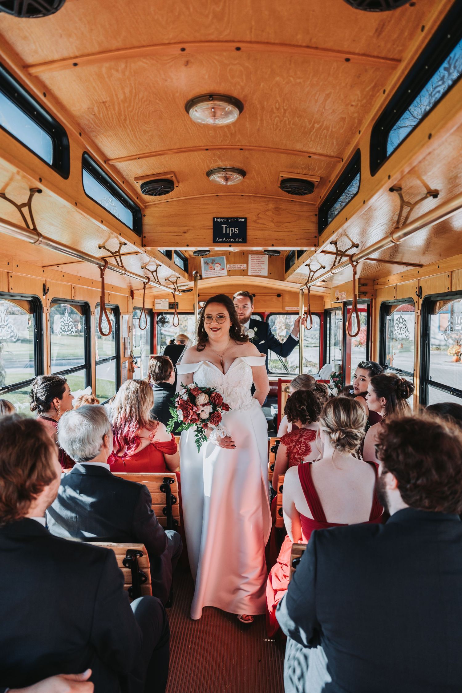 Wedding party riding in a vintage trolley bus with wooden interior panels.