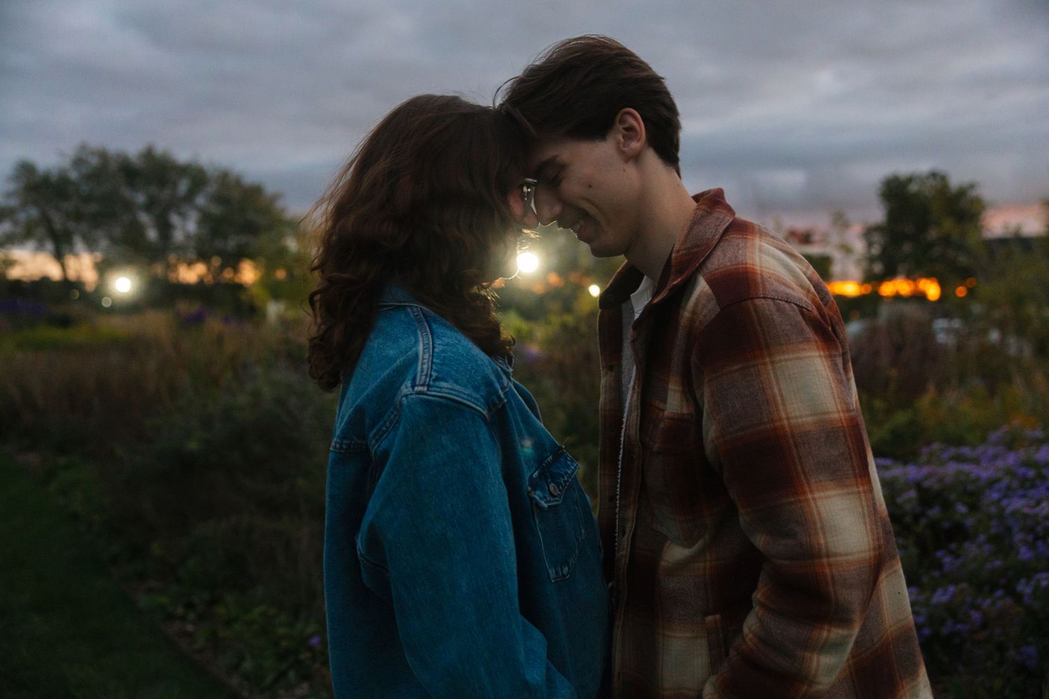 A young couple shares a romantic moment at dusk in a garden, foreheads touching tenderly.
