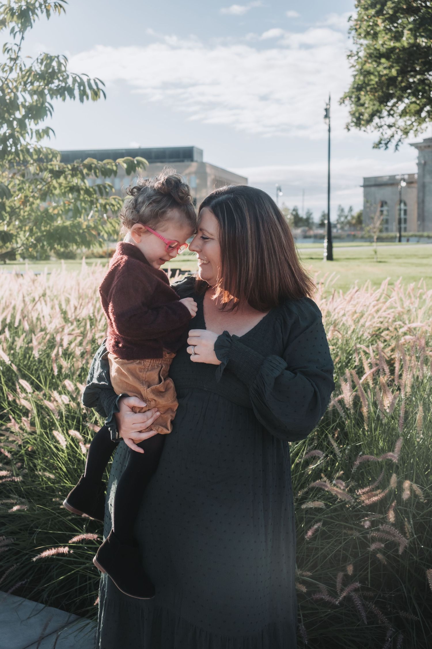 Tender moment between parent and child in a field of ornamental grasses with buildings in background.