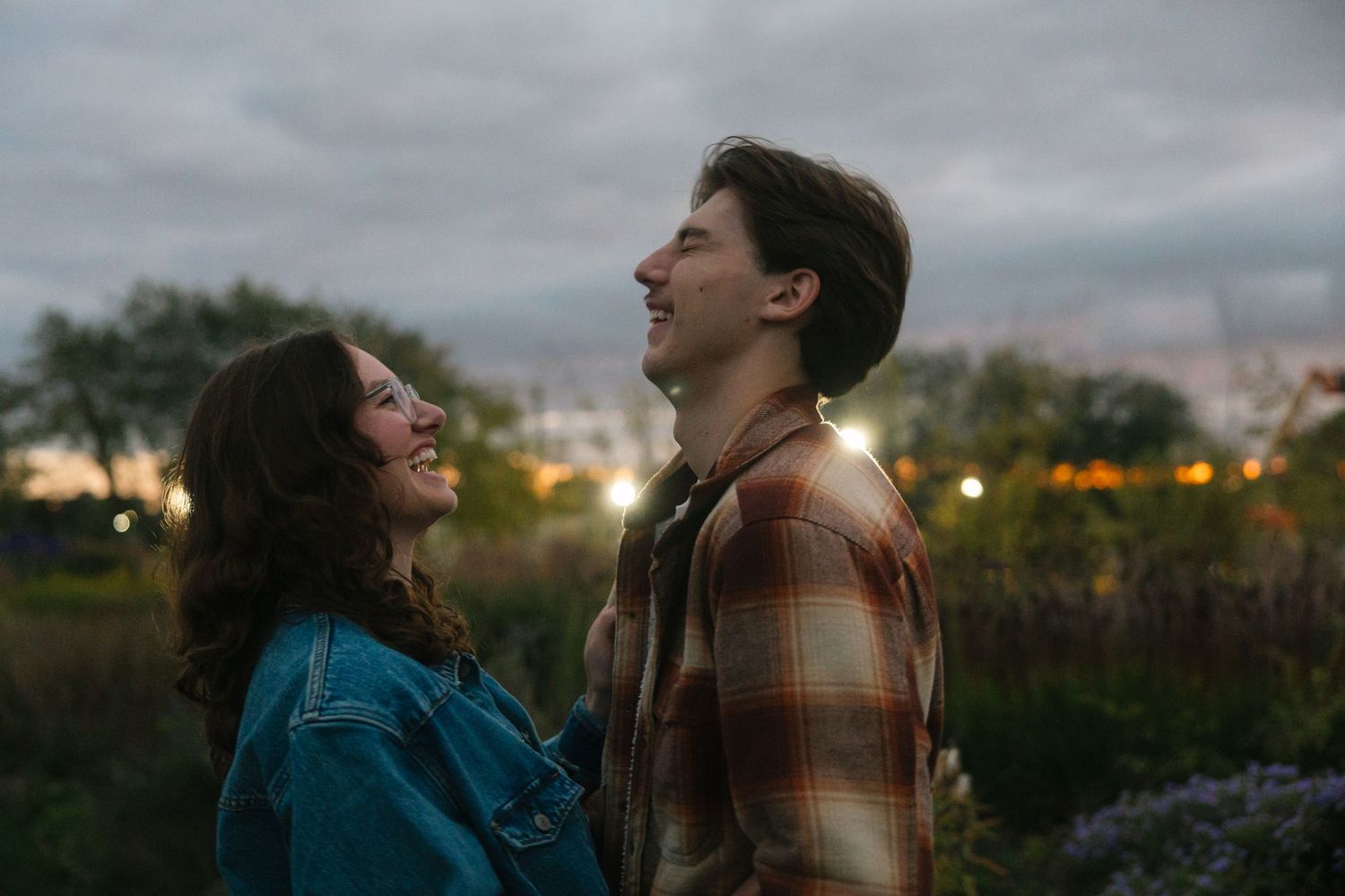 Happy young couple smiling and laughing together outdoors at dusk with city lights in the background.