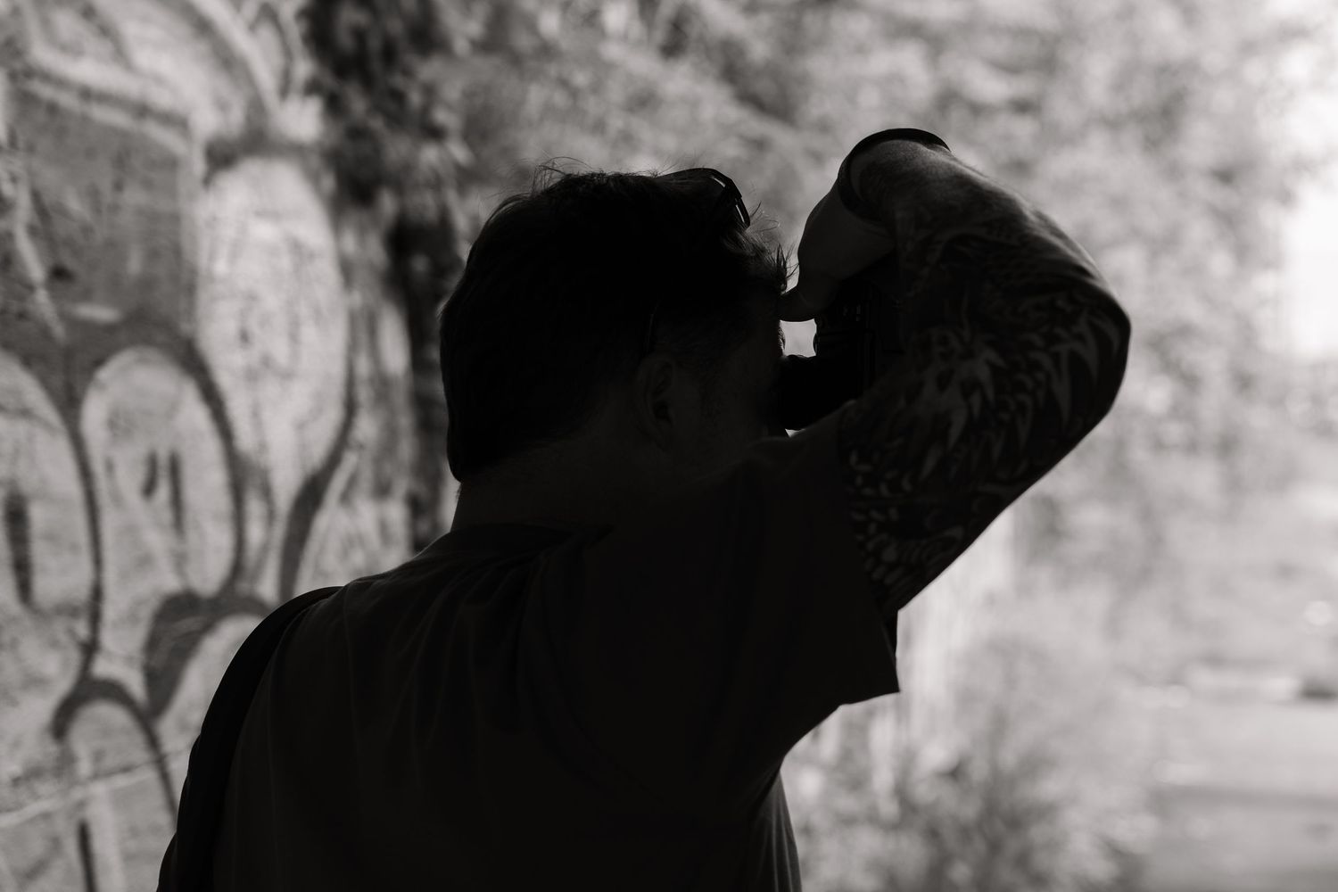 Black and white photo of a man with hand raised to his head near a graffiti wall.