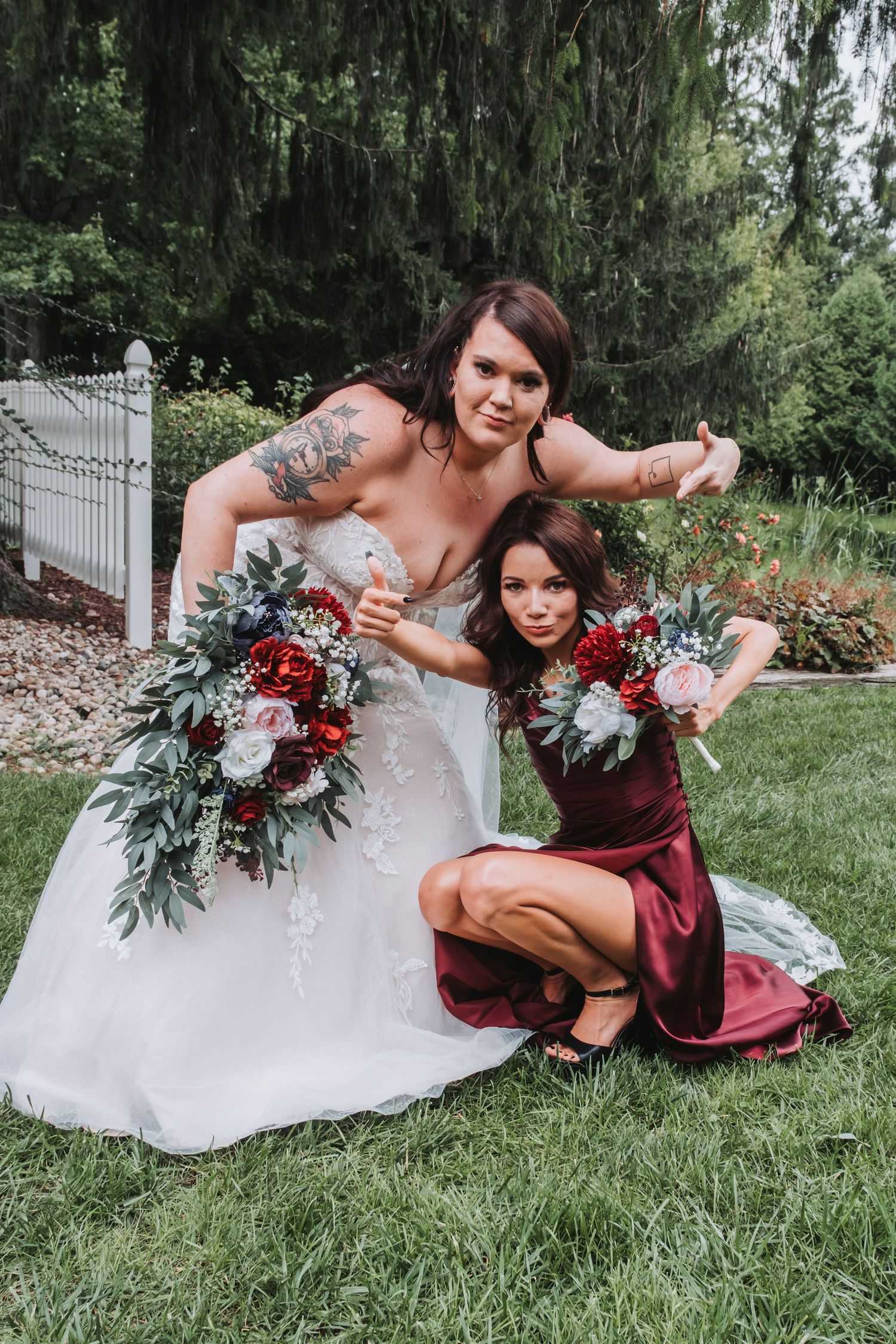 Wedding party members pose with bouquets featuring burgundy and white flowers with greenery.