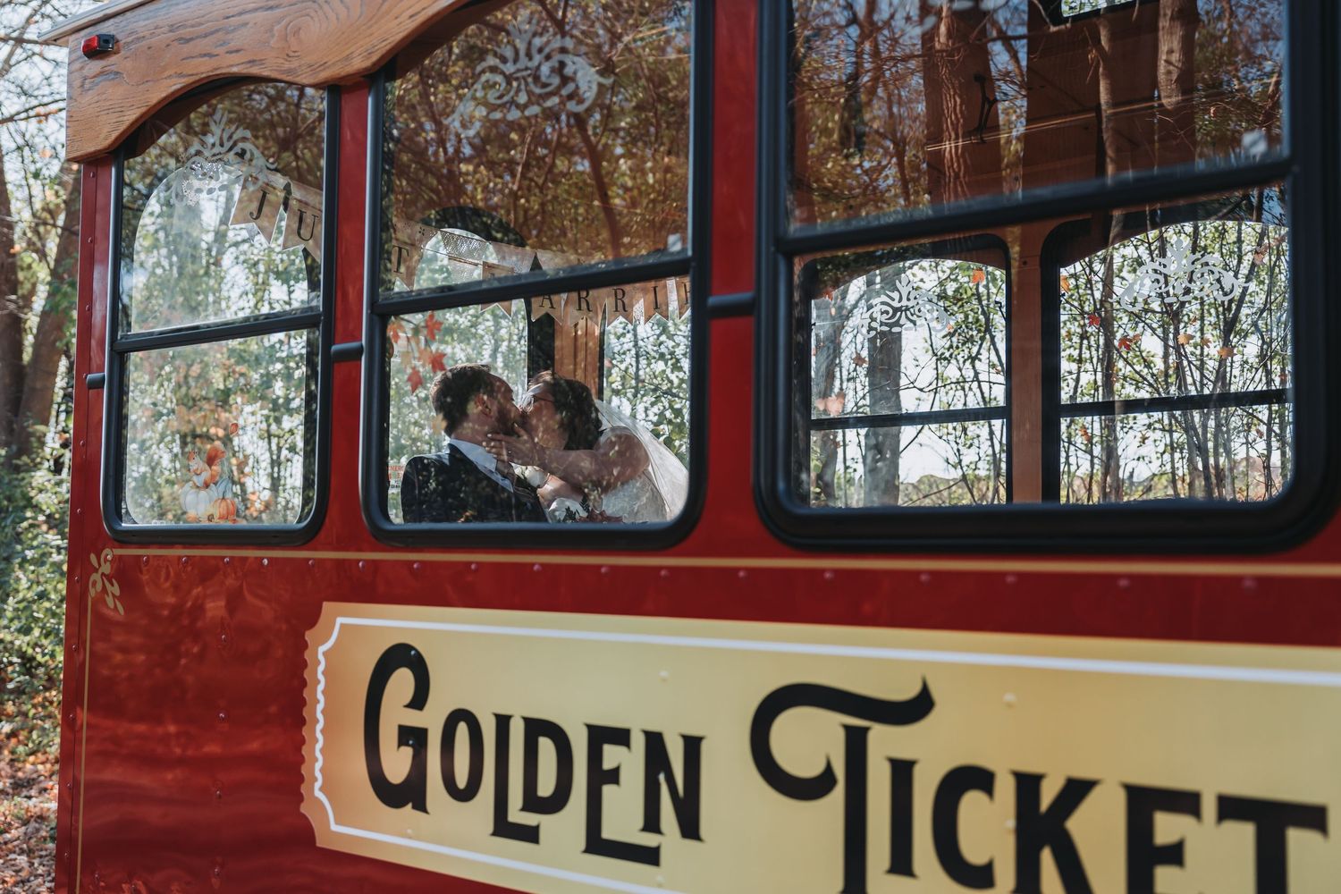 Red tour bus with 'Golden Ticket' text visible through trees in autumn setting.