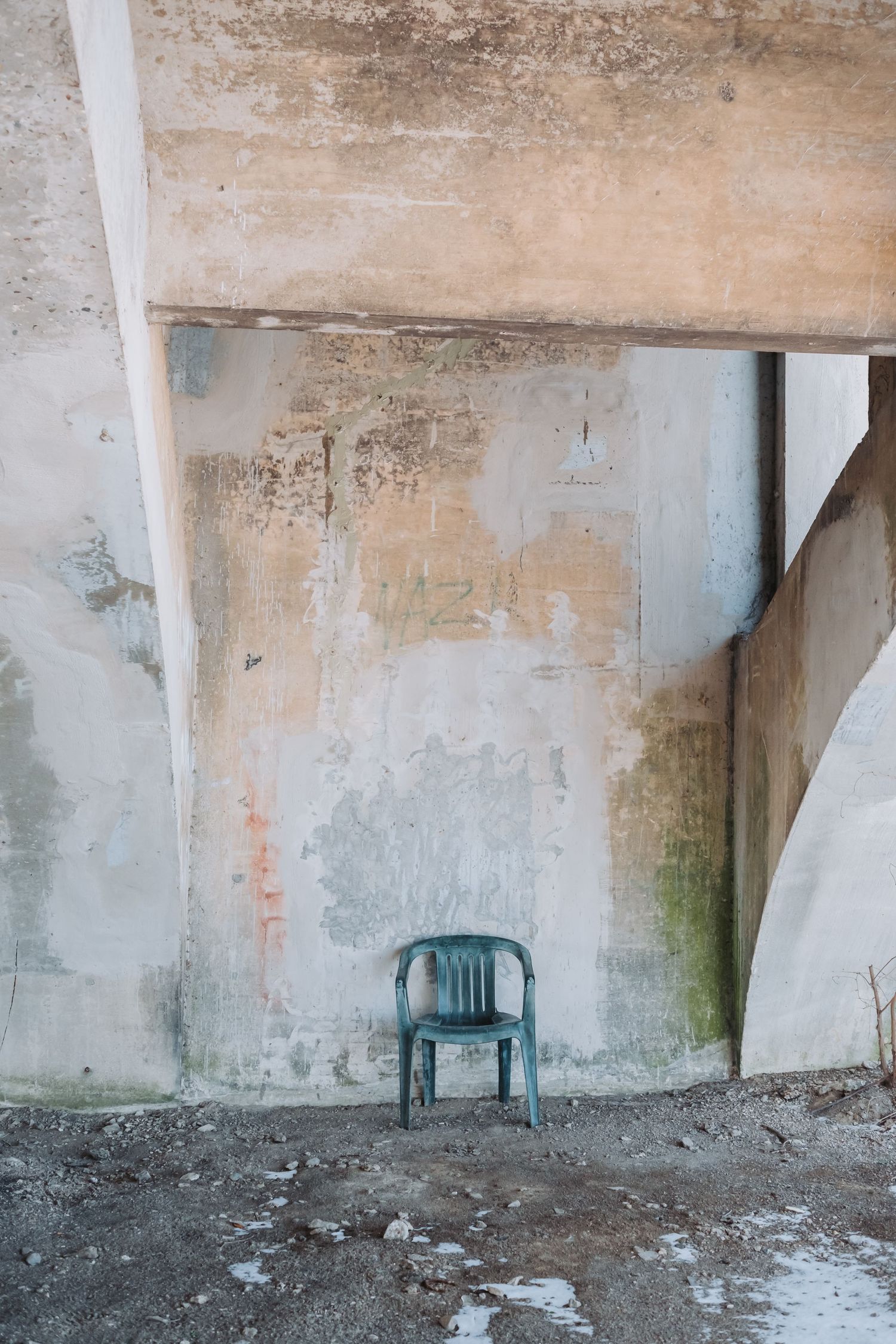 Weathered concrete wall with exposed patches and a blue chair against it.