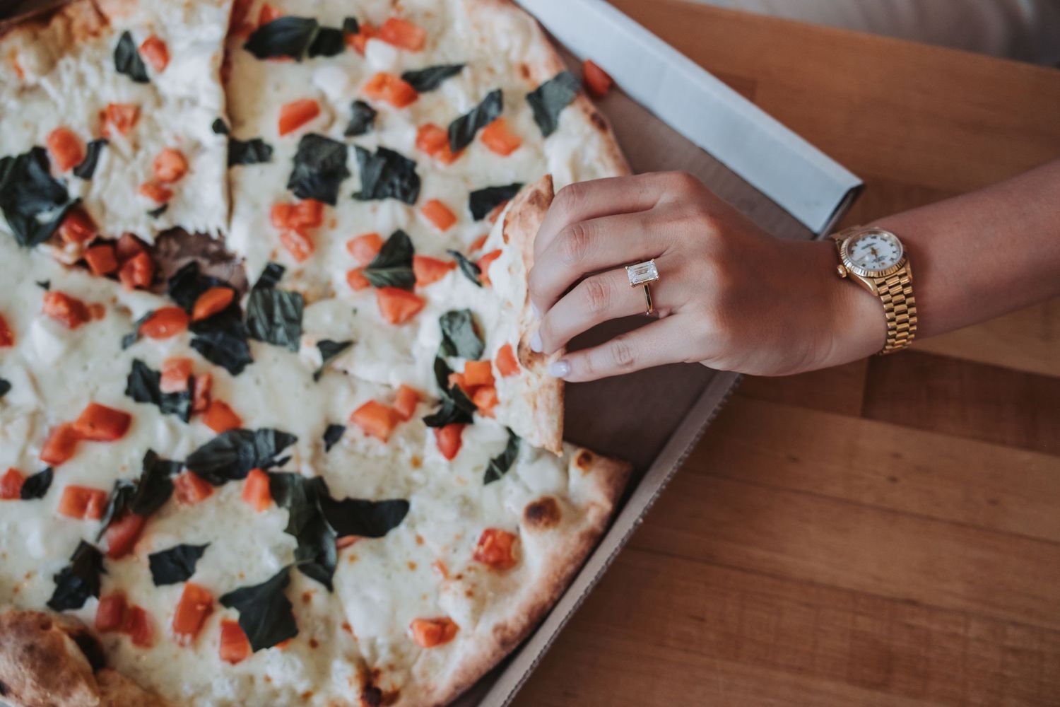 Hands reaching for slices of a gourmet pizza topped with fresh herbs and vegetables.