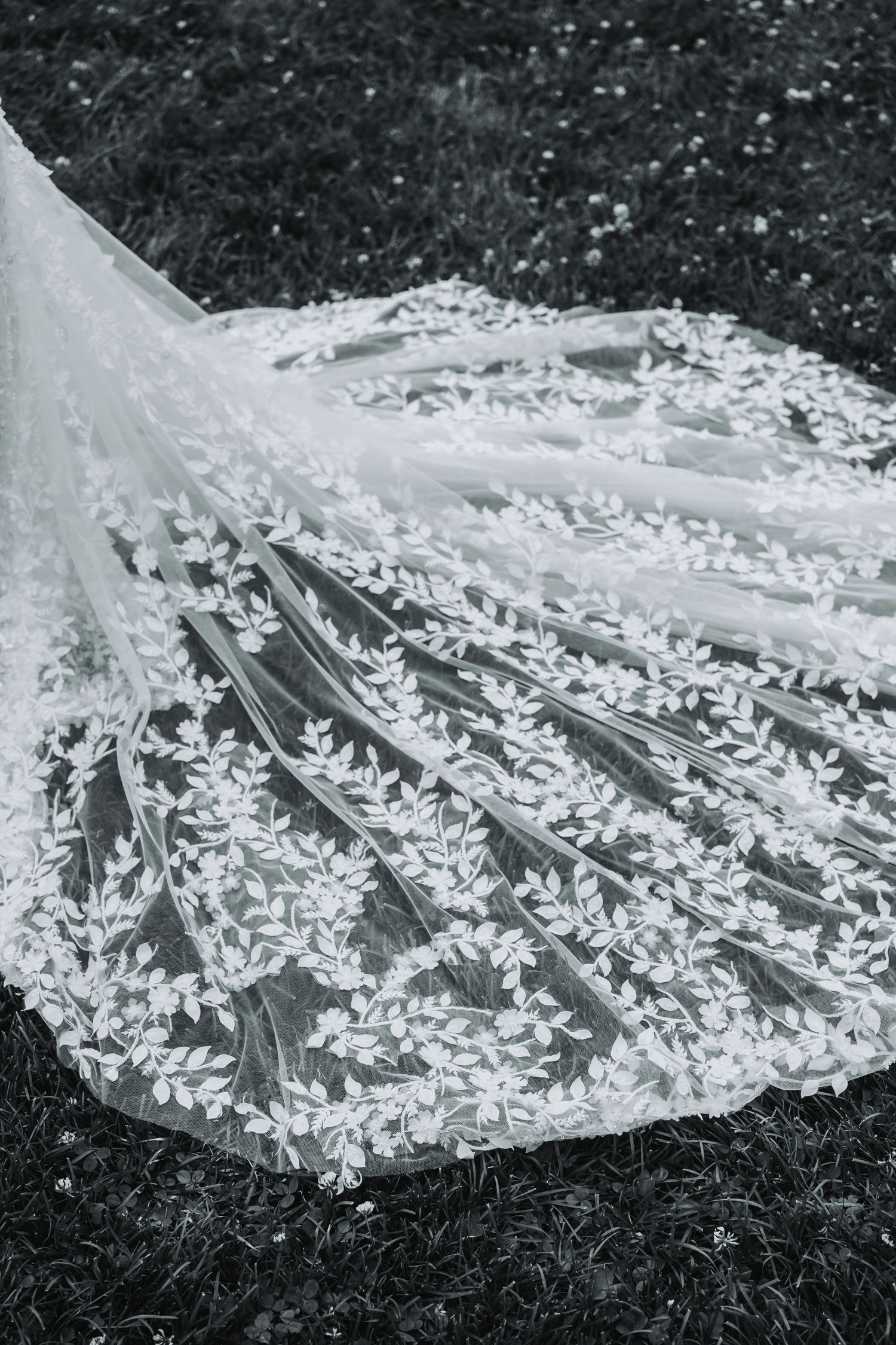 Black and white photograph showing delicate floral lace details on a wedding dress train.