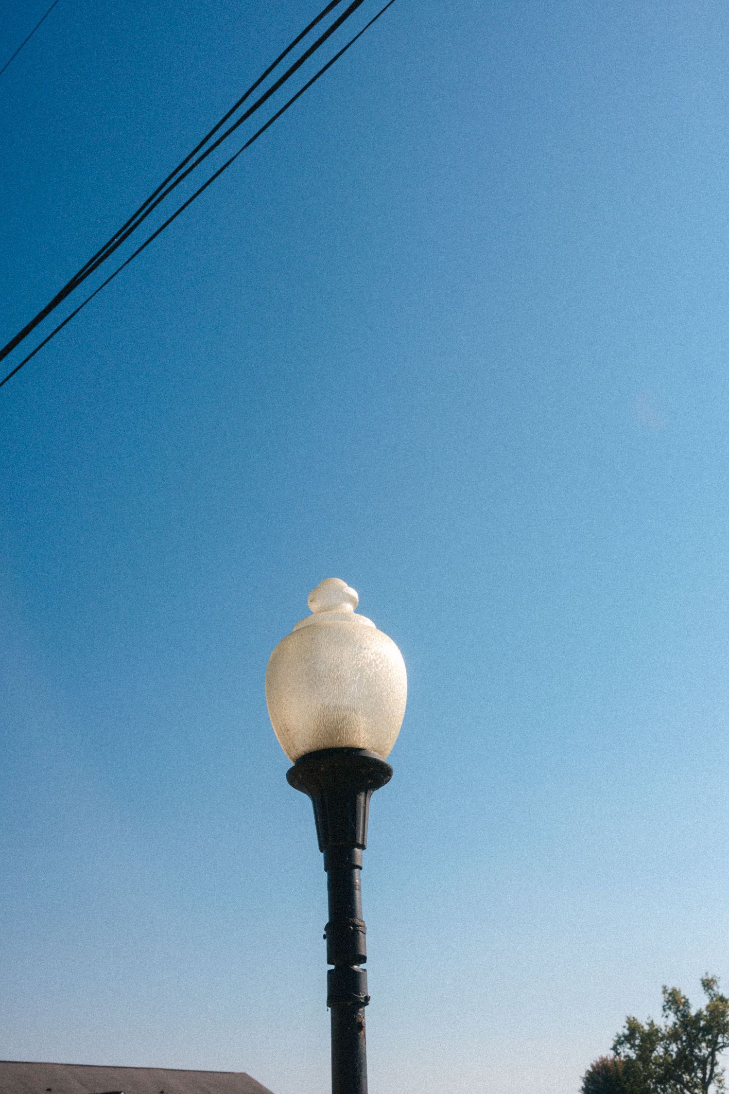 A vintage-style street lamp post stands against a bright blue sky with power lines visible.