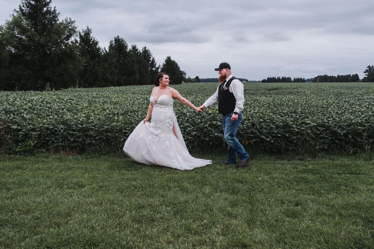 Couple in wedding attire sitting in green field.