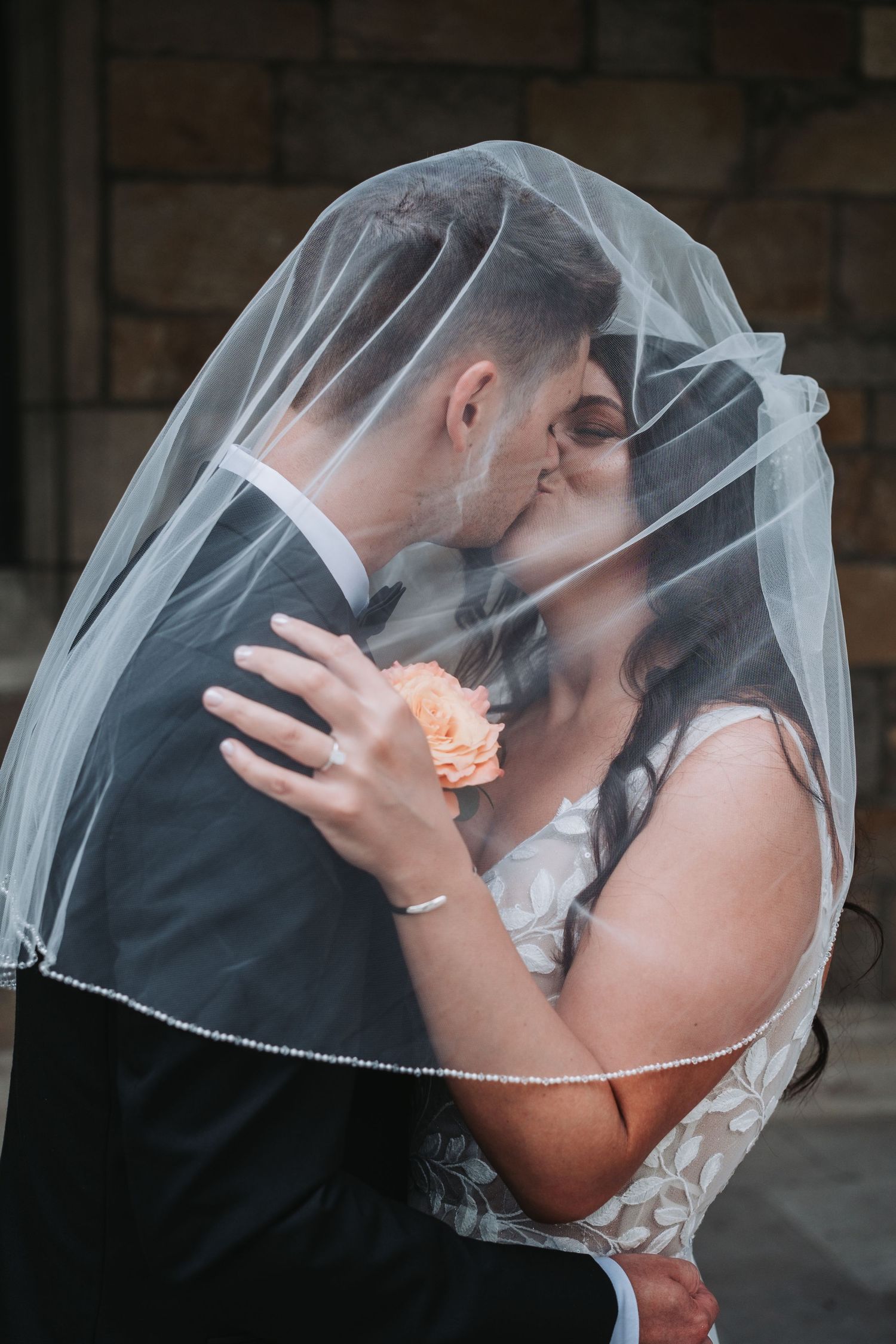 Romantic moment under flowing white wedding veil with peach flower accent.