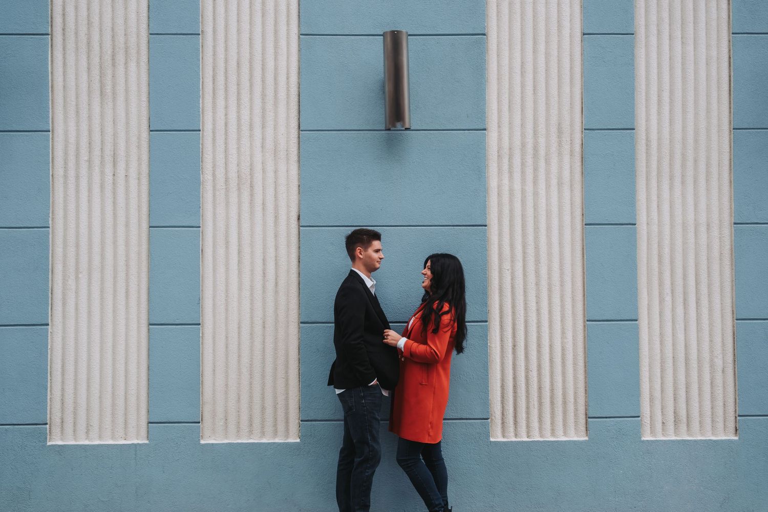 Couple sharing a romantic moment in front of a blue wall with white columns.