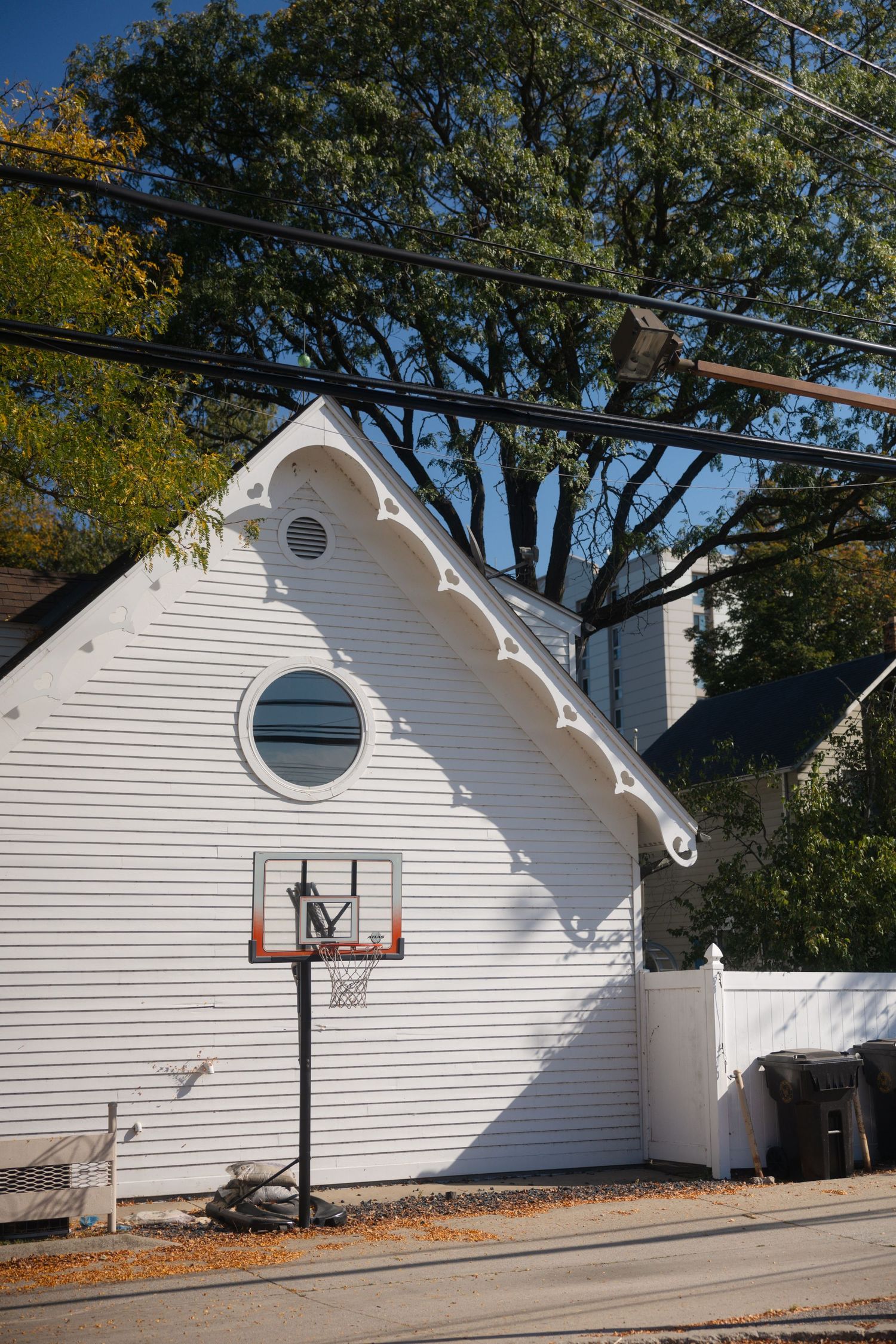White curved wall building with basketball hoop mounted on exterior and round window features in residential setting.