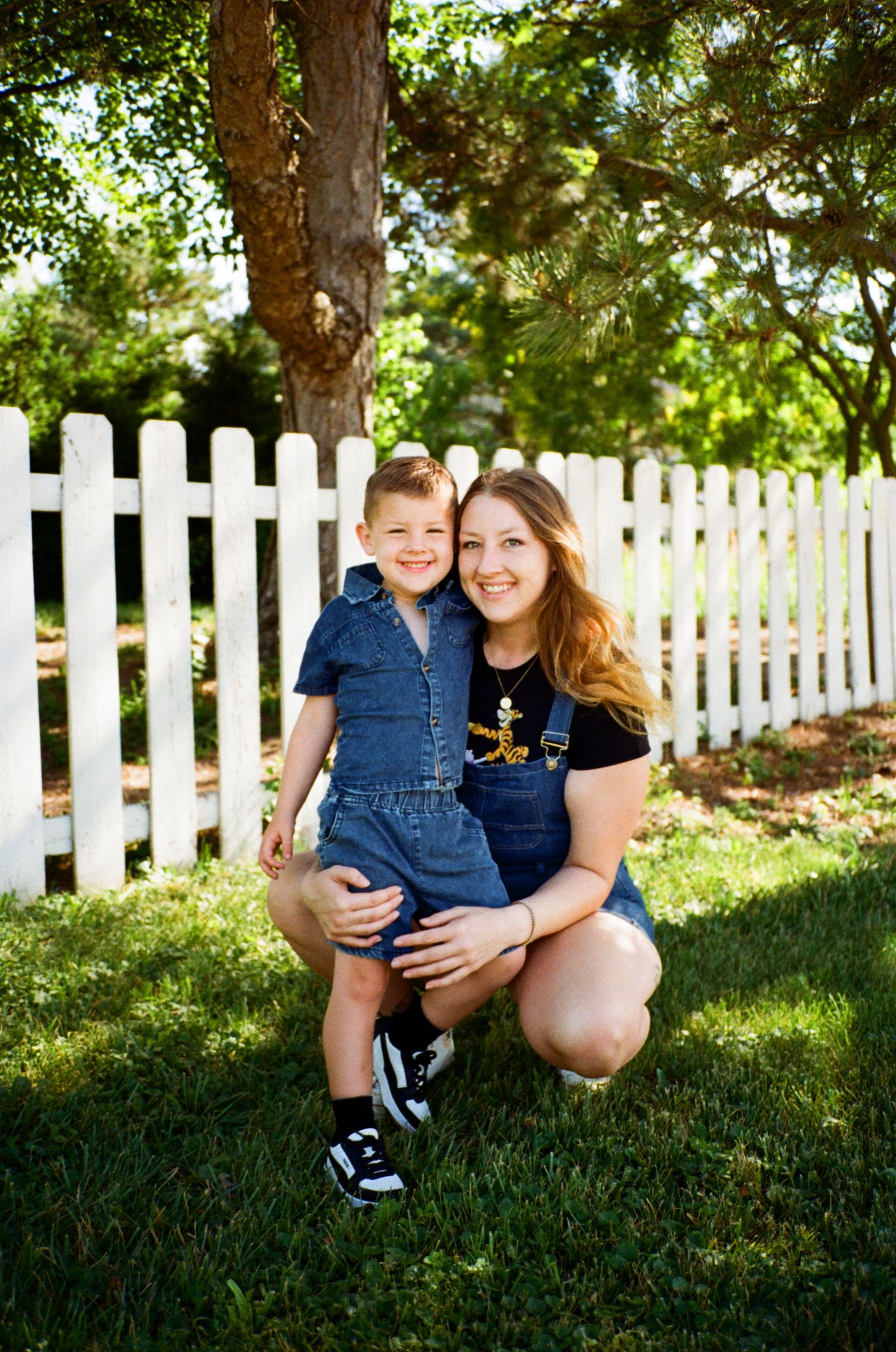 Family portrait session by a white picket fence in dappled sunlight.
