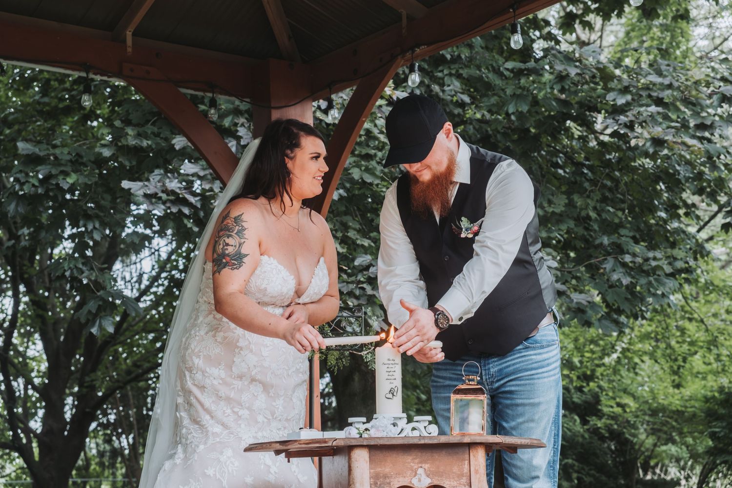 Wedding couple cutting their cake together under a wooden pavilion.