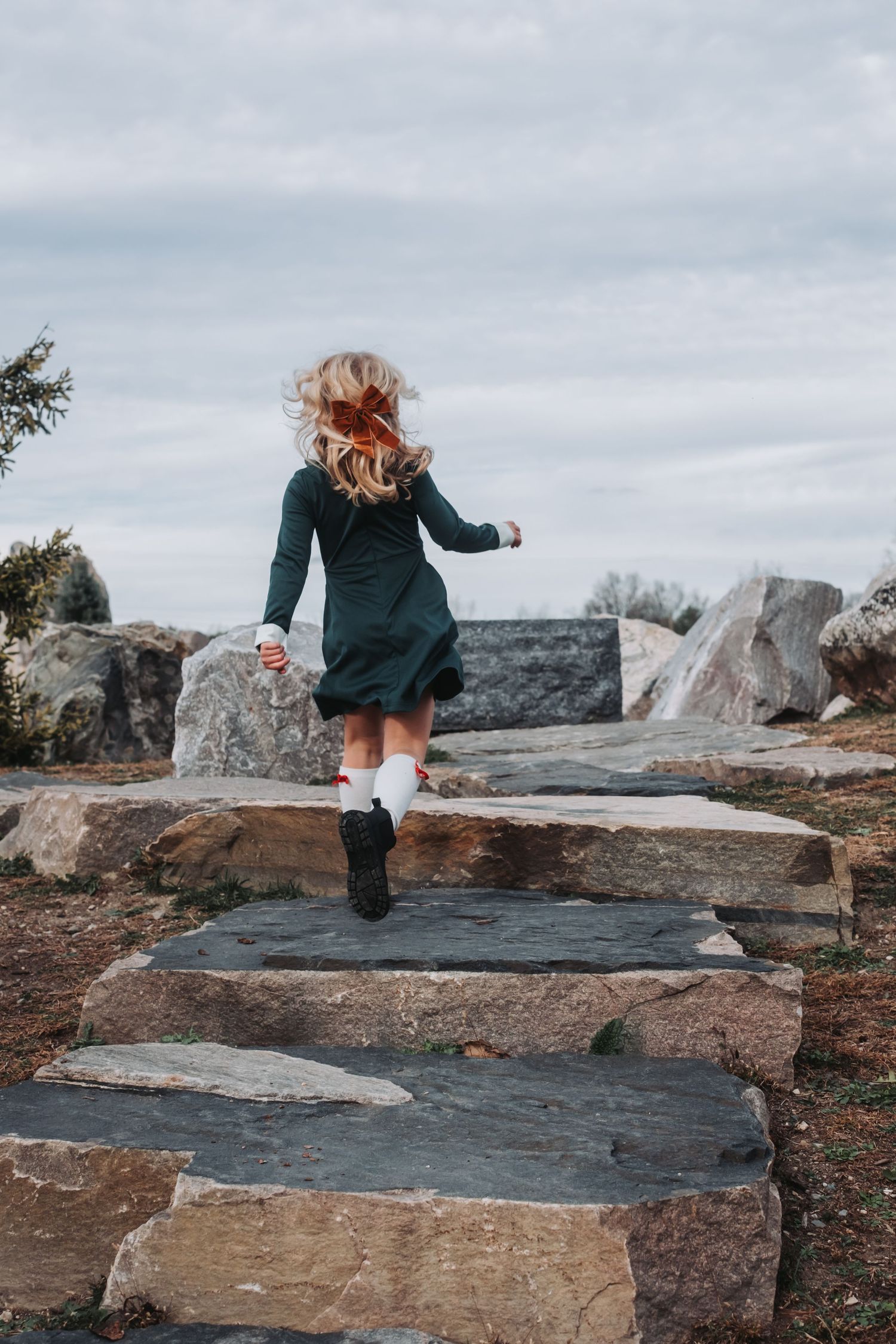 A small child in a dark dress climbs stone steps outdoors.