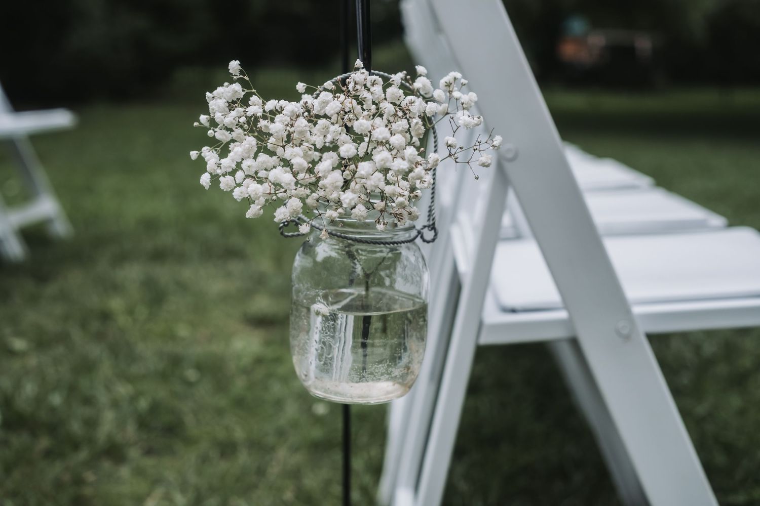 Mason jar filled with delicate baby's breath flowers hanging on white ceremony chair.