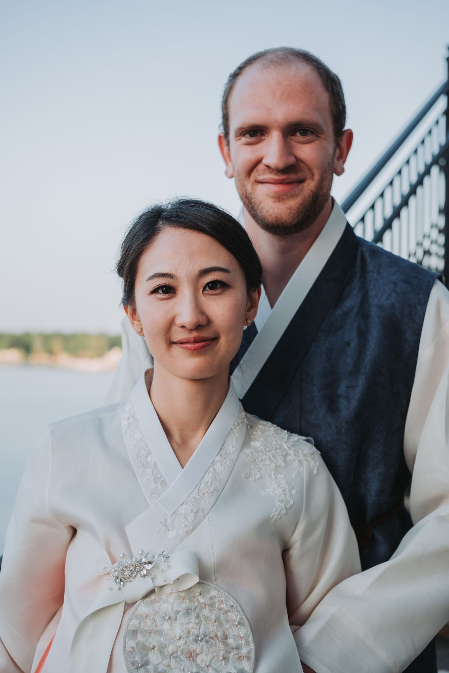 A couple poses together in formal attire with the bride wearing a traditional white hanbok dress.