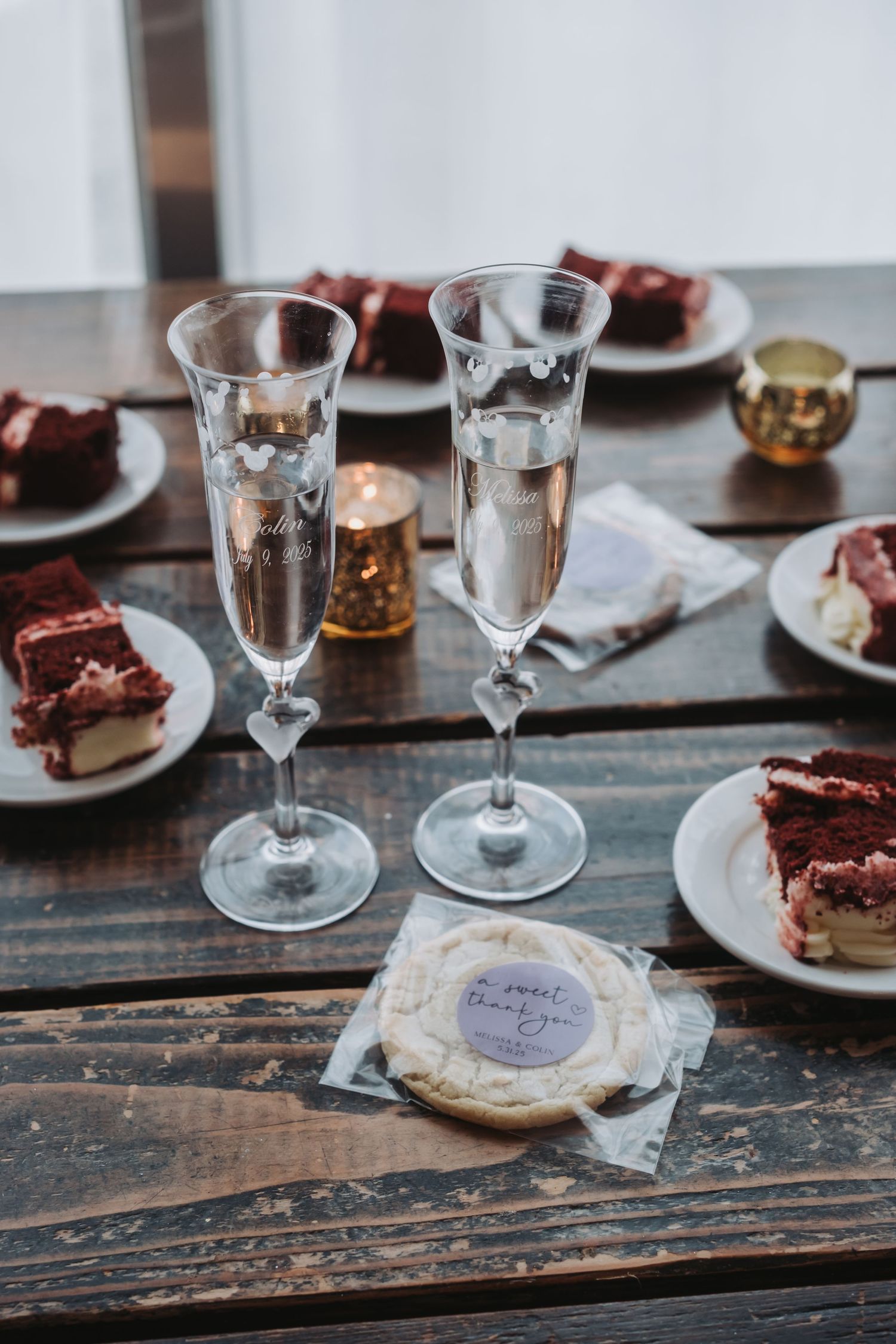 Wine glasses and dessert plates arranged on a rustic wooden table for a celebration.