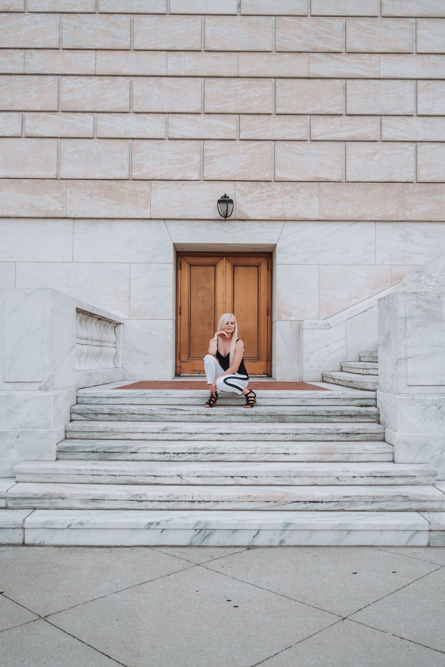 Woman sitting on marble steps of a grand building with wooden doors and stone architecture.