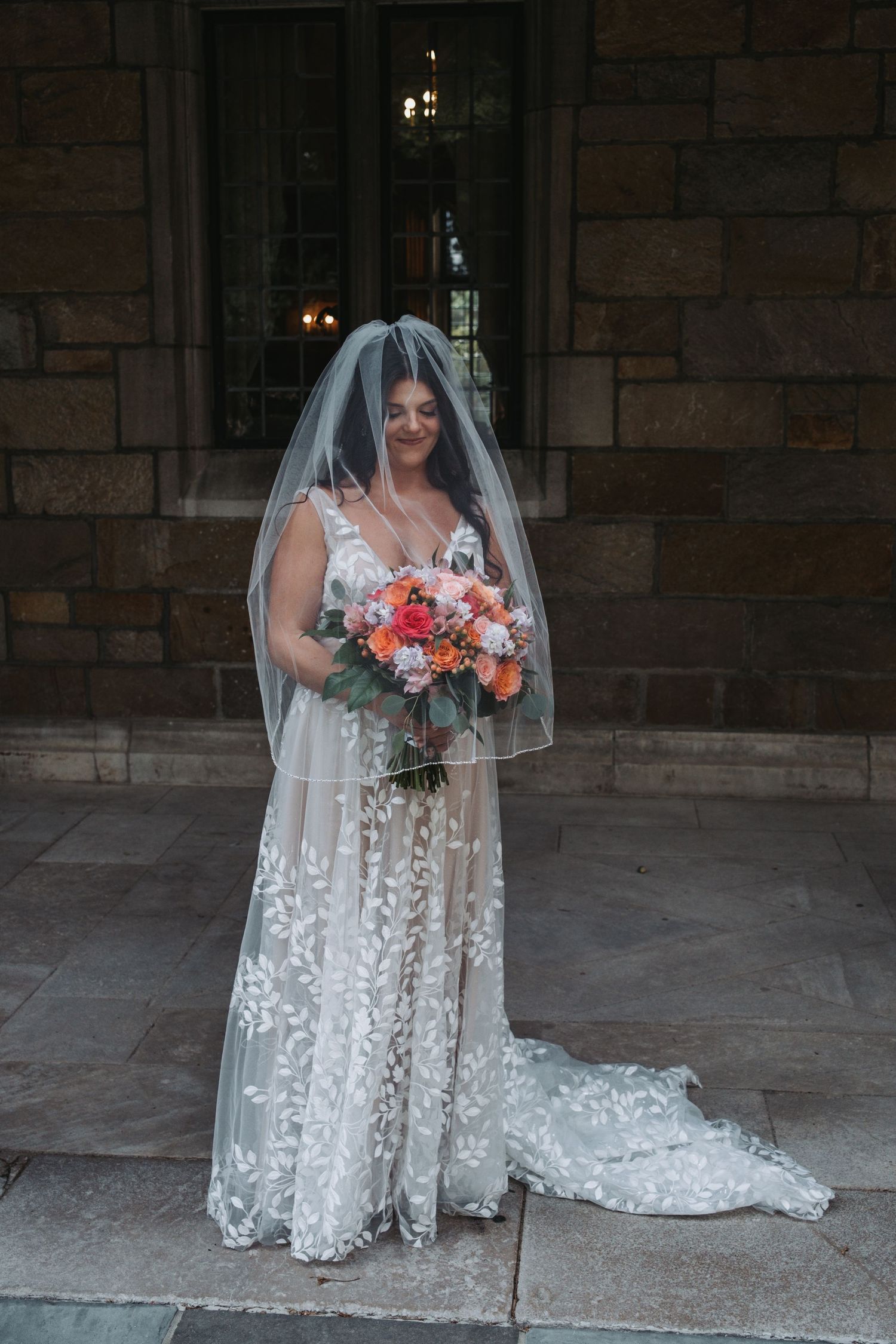 Bridal portrait showcasing elegant lace dress and colorful bouquet against stone backdrop.