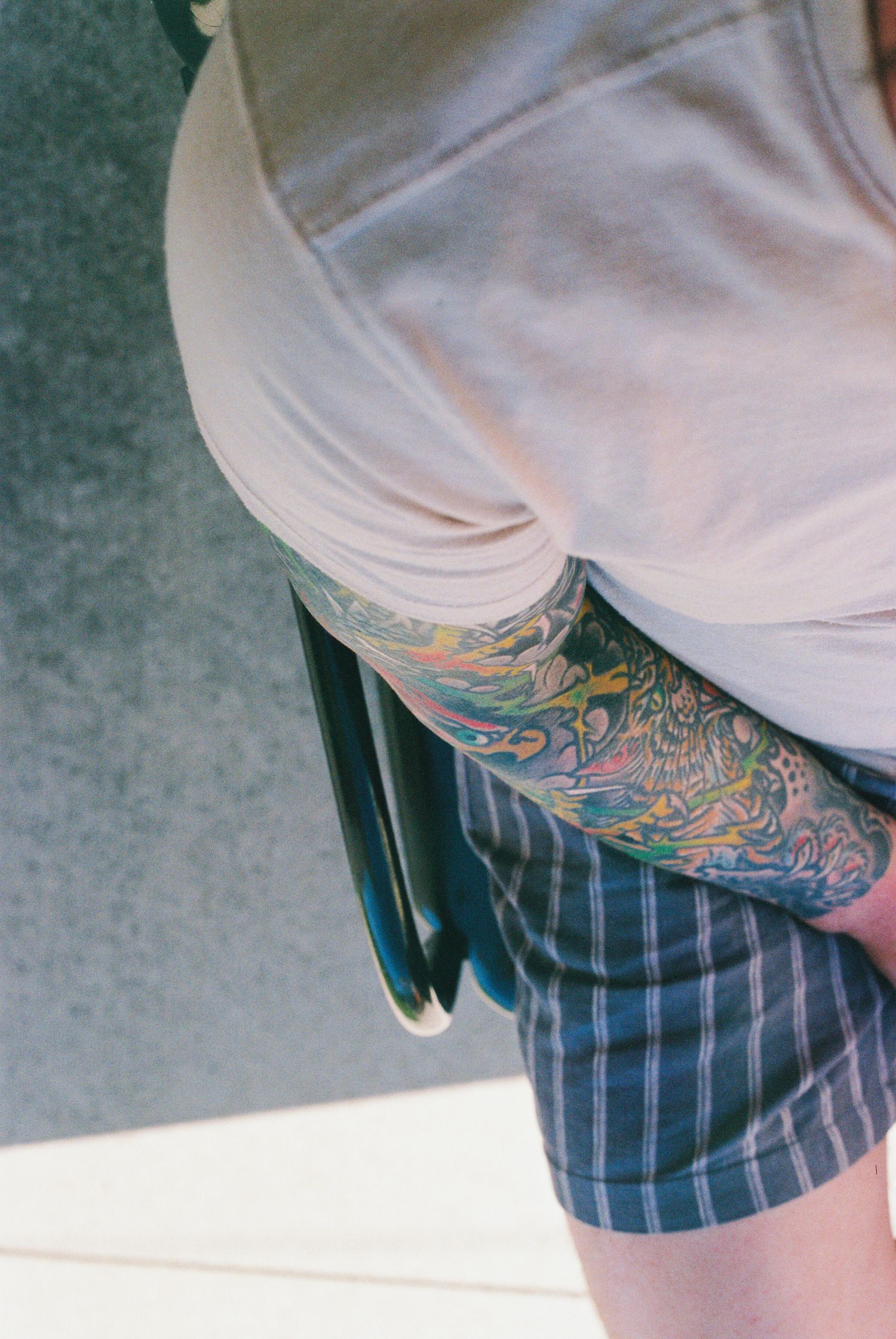 Colorful sleeve tattoo visible beneath white shirt and plaid shorts.