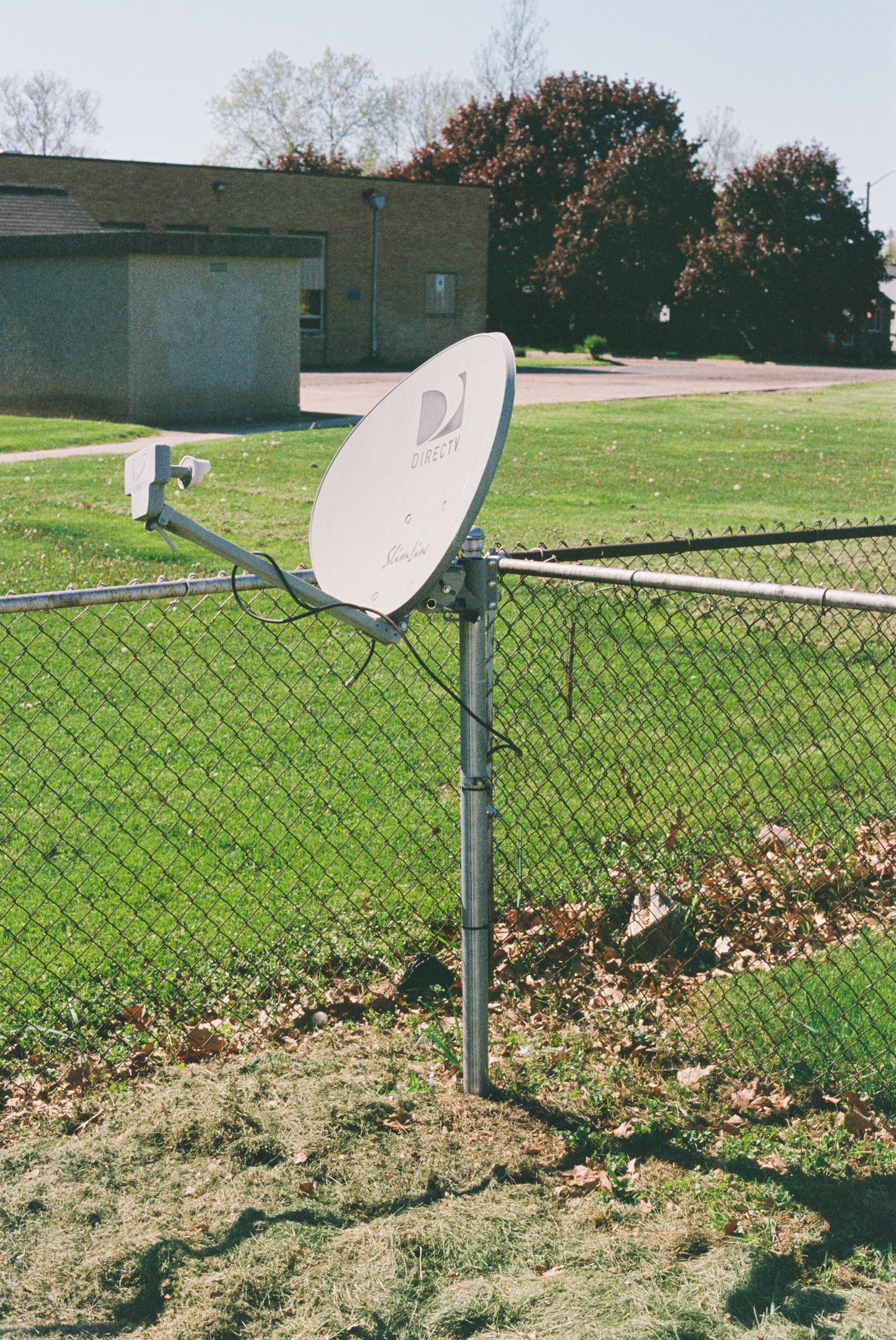 Satellite dish mounted on chain link fence in grassy field.