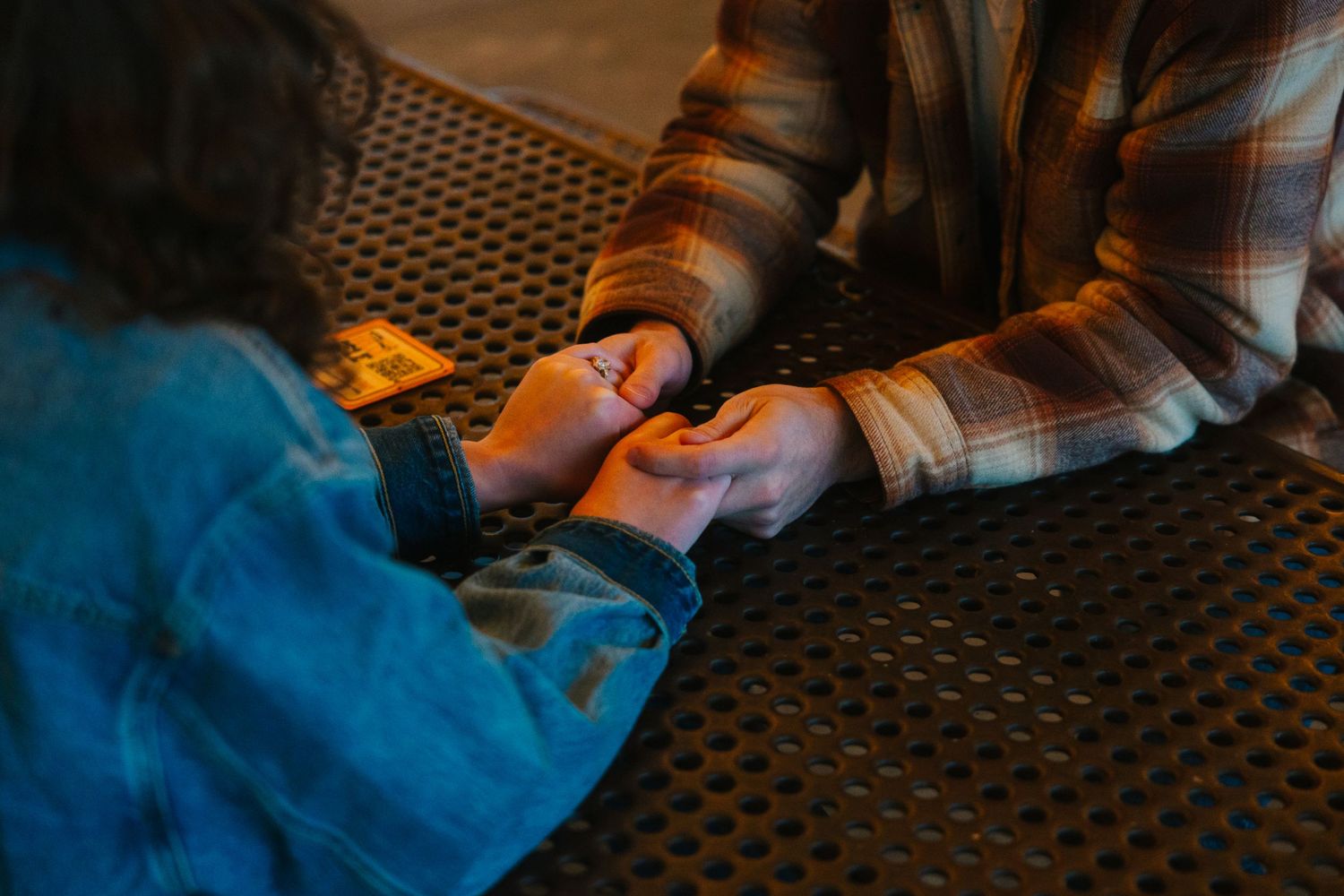 Two people holding hands across a table in warm evening light.