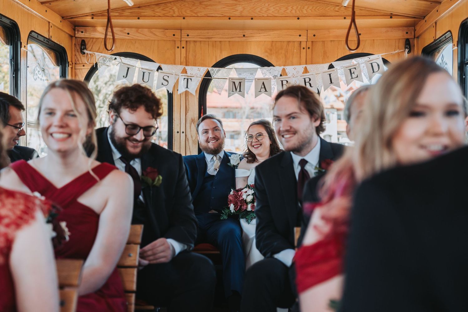 Wedding guests smiling and celebrating inside a trolley decorated with a Just Married banner.