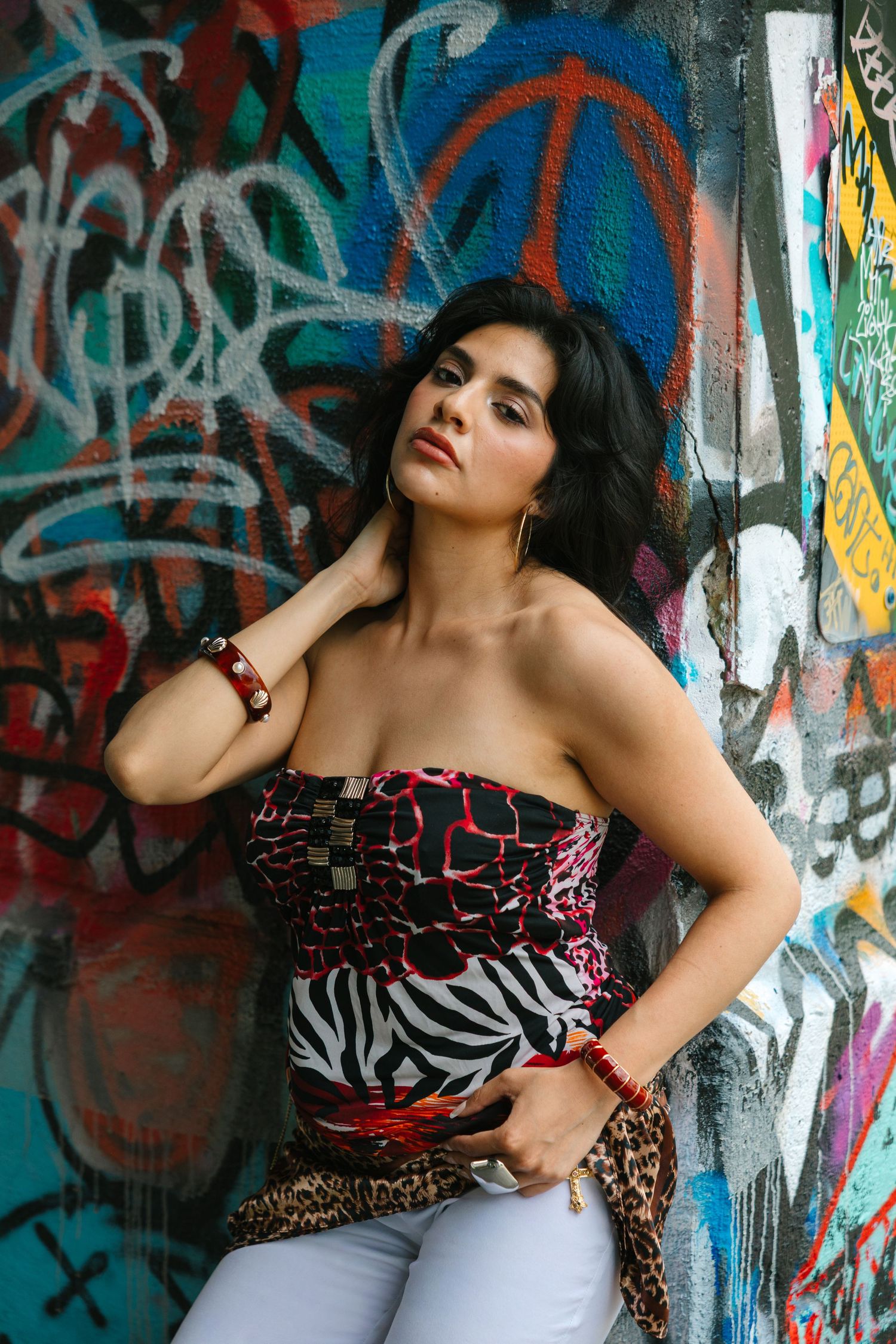 Brunette woman in strapless animal print top posing confidently against vibrant graffiti wall.