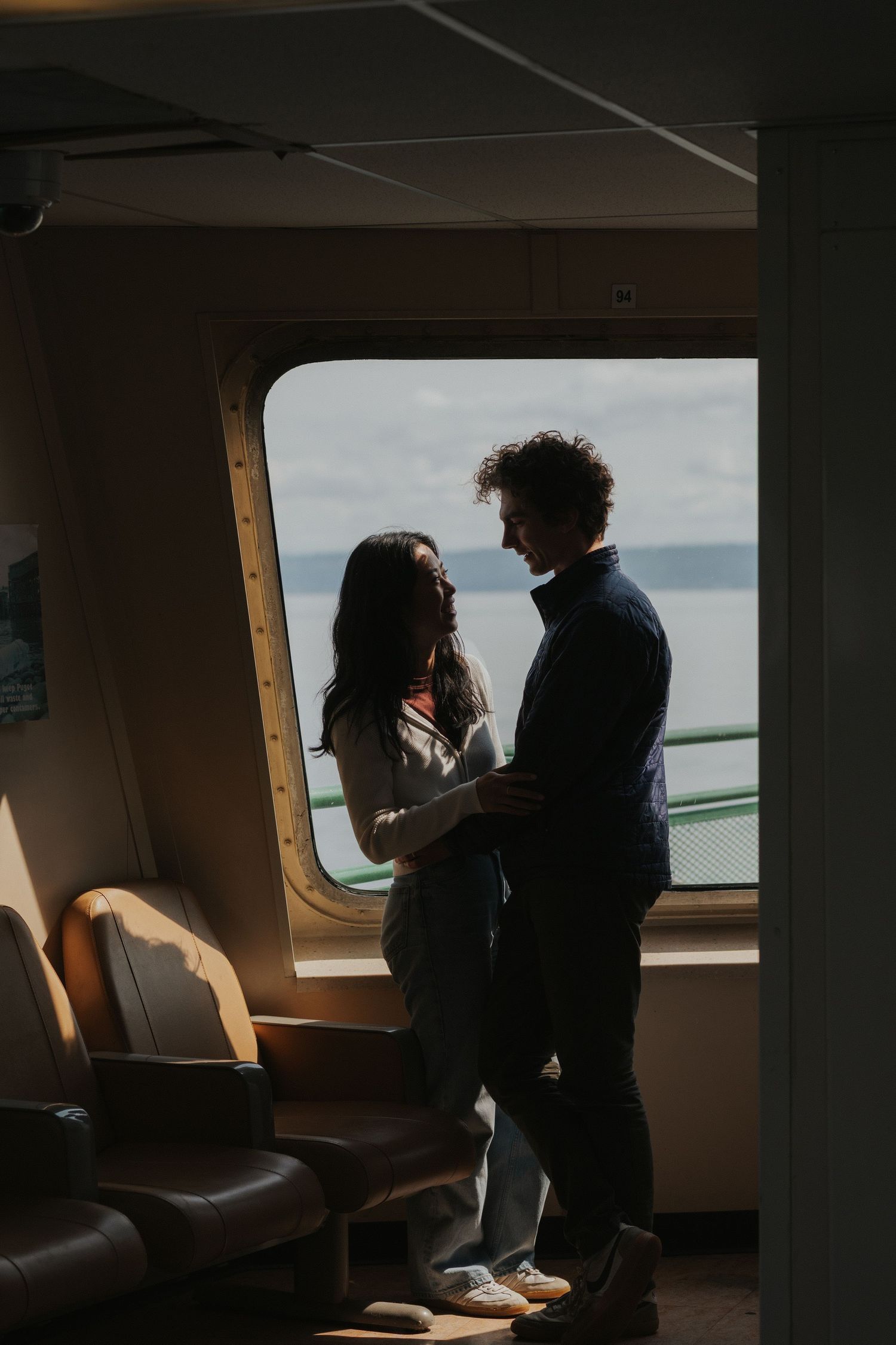Silhouetted figures in tender embrace near window of boat cabin.