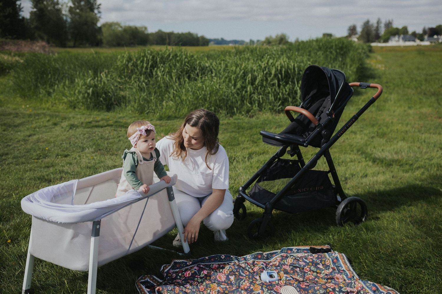 Outdoor picnic setup with blanket and stroller on green grass.
