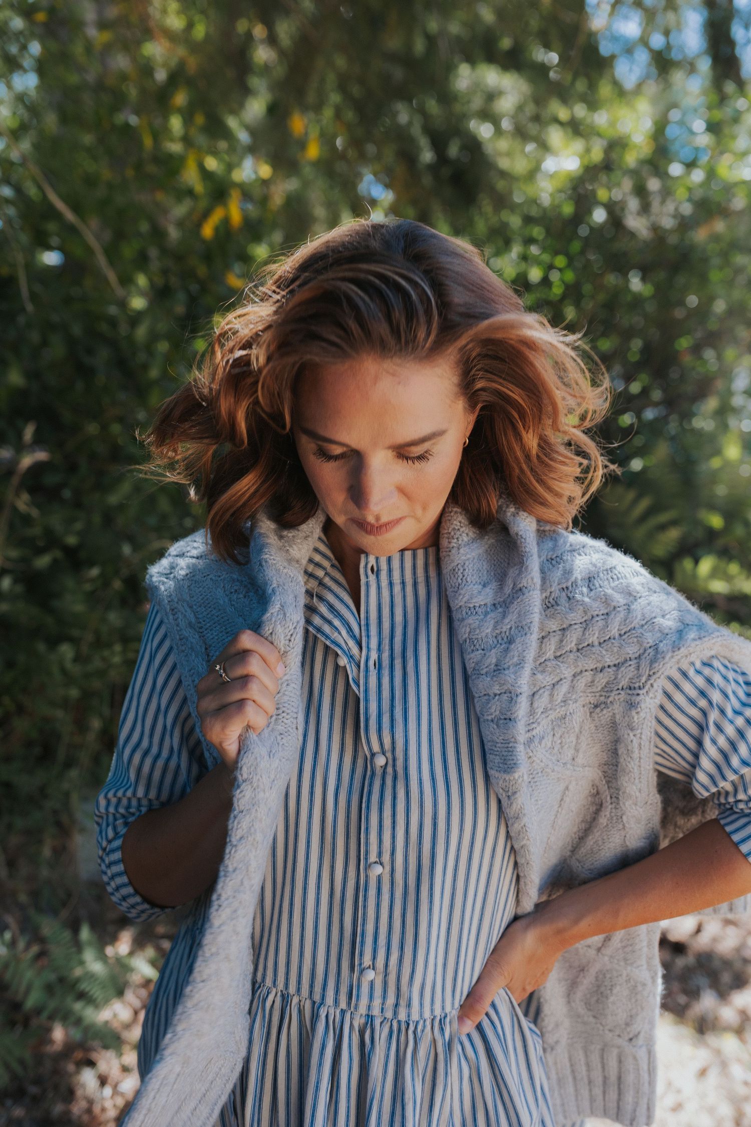 A close-up fashion photo showing a striped button-up shirt paired with a knit cardigan.