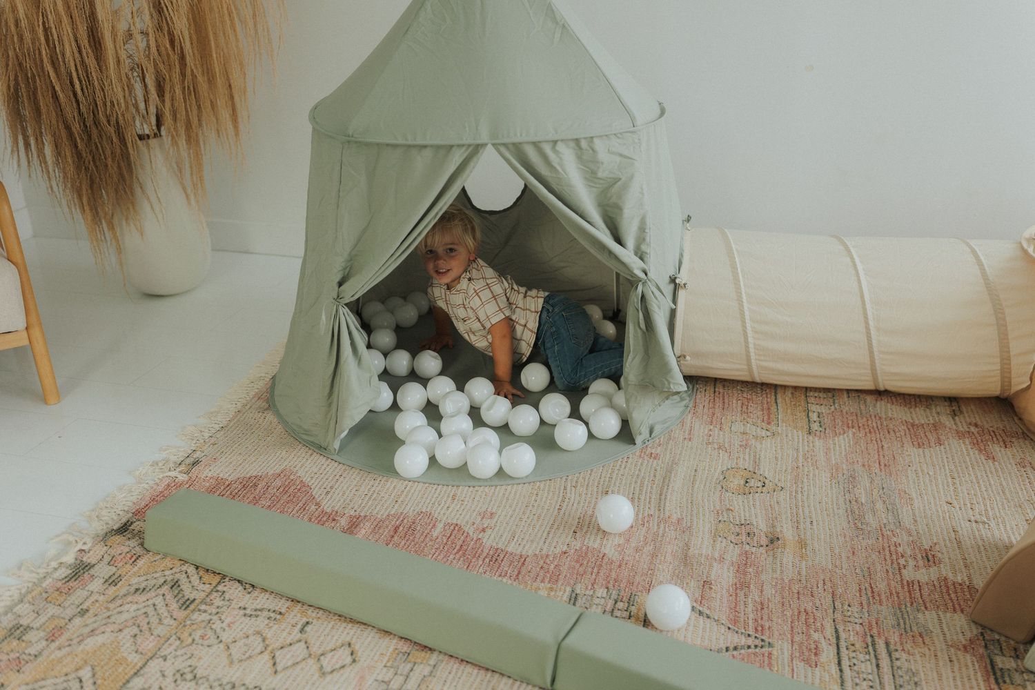Minimalist playroom setup with sage green tent and white pom pom decorations.