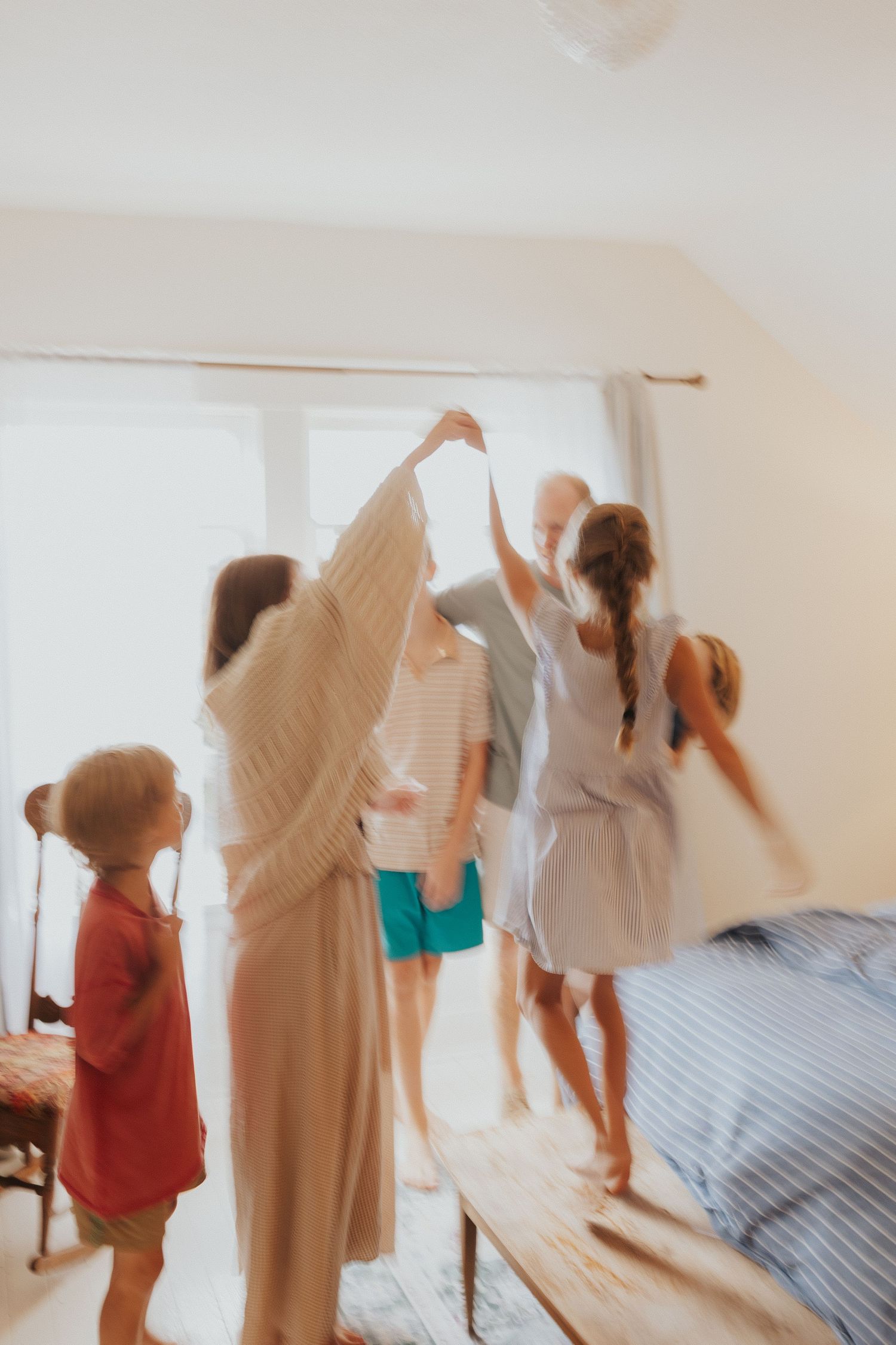 Motion-blurred photos of people playing and jumping in a bright bedroom.