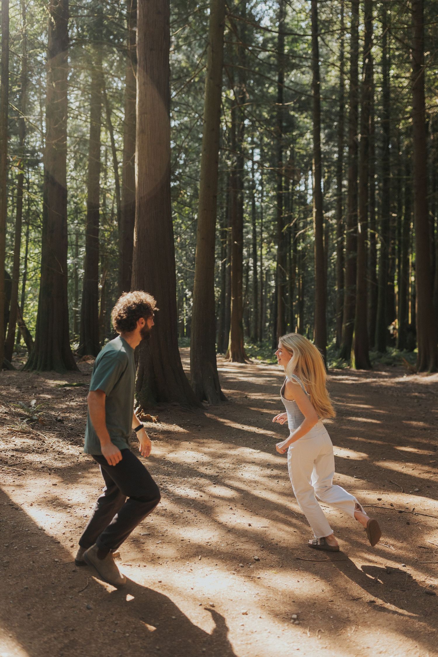 A couple performs a synchronized dance move in a sunlit forest clearing surrounded by tall trees.