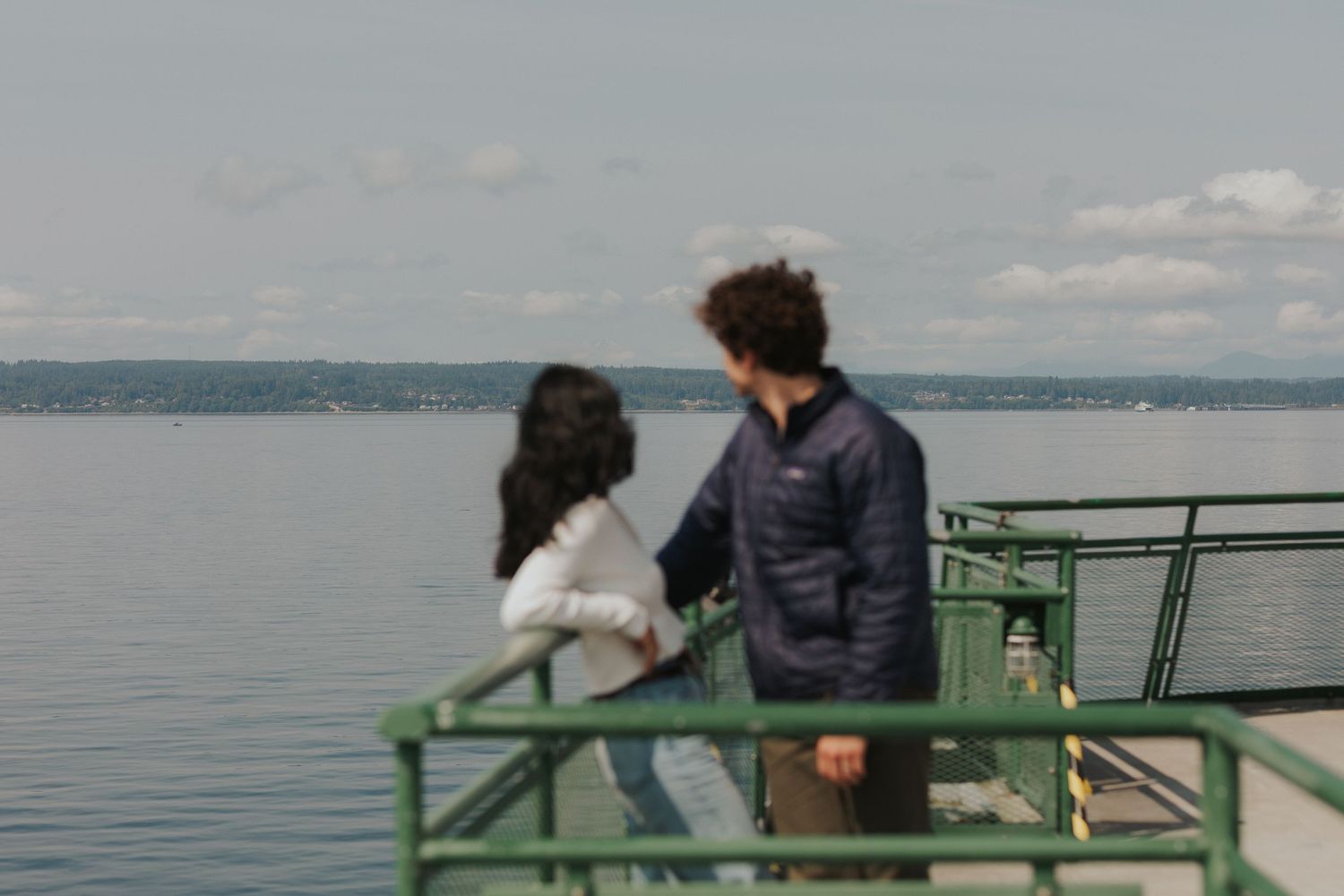 A couple enjoys a peaceful moment on a waterfront deck with distant shoreline visible.