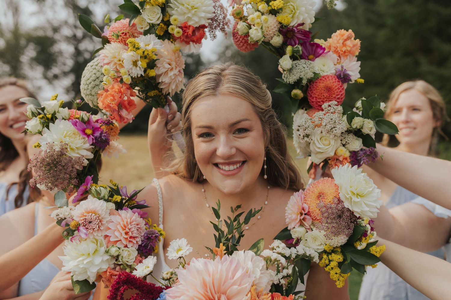 Colorful floral crowns and bouquets adorn a wedding party in an outdoor setting.