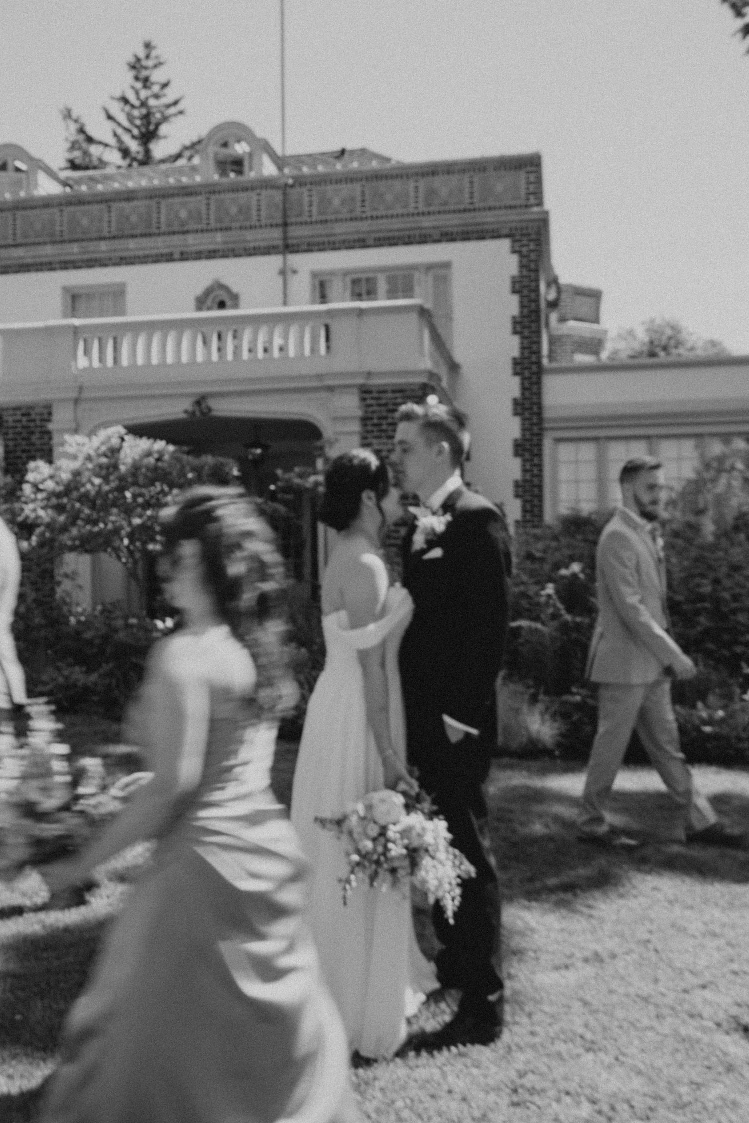 Black and white photo of wedding party walking in sequence outside a historic building.