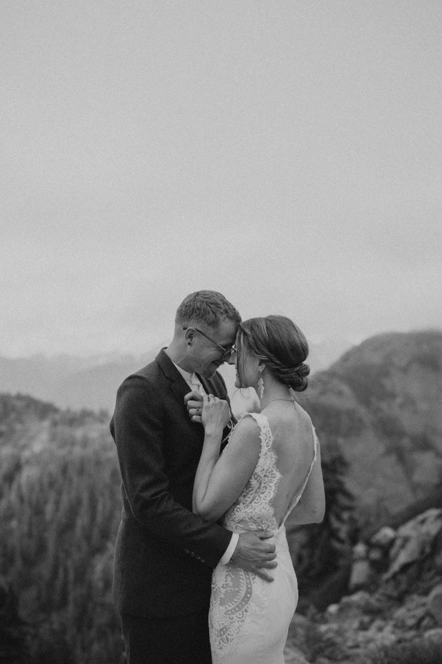 Black and white photo of newlyweds embracing against a mountainous backdrop.
