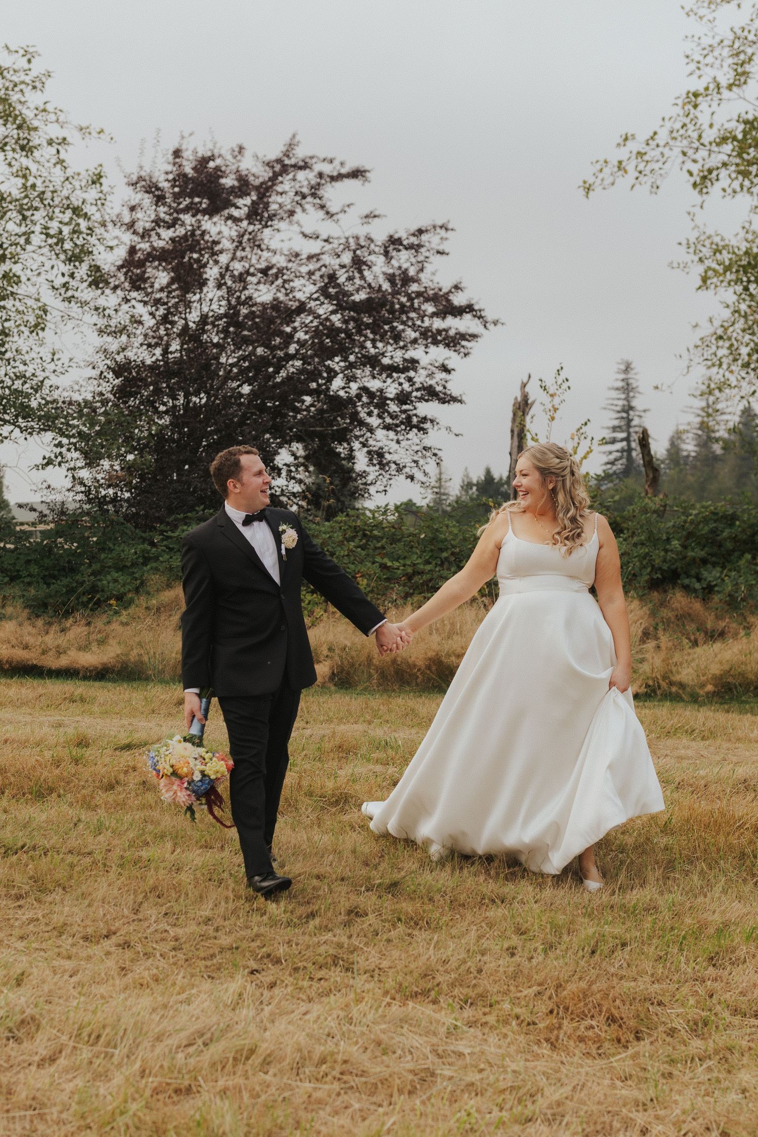 A playful wedding couple interacts on a grassy hillside during their photo session.