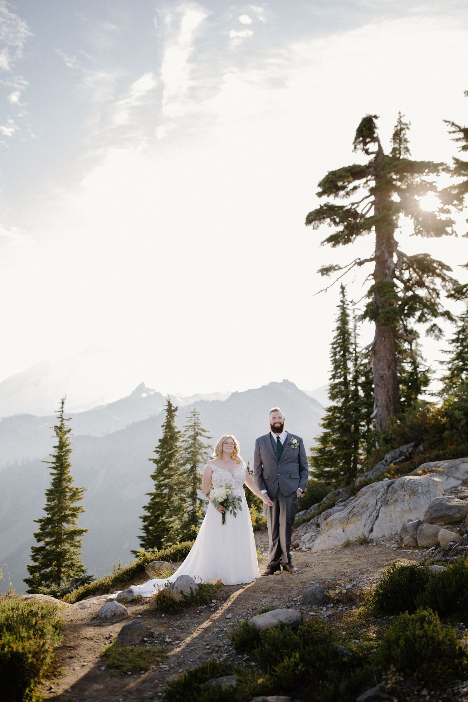 Couple poses on rocky mountain summit during sunset wedding photoshoot.