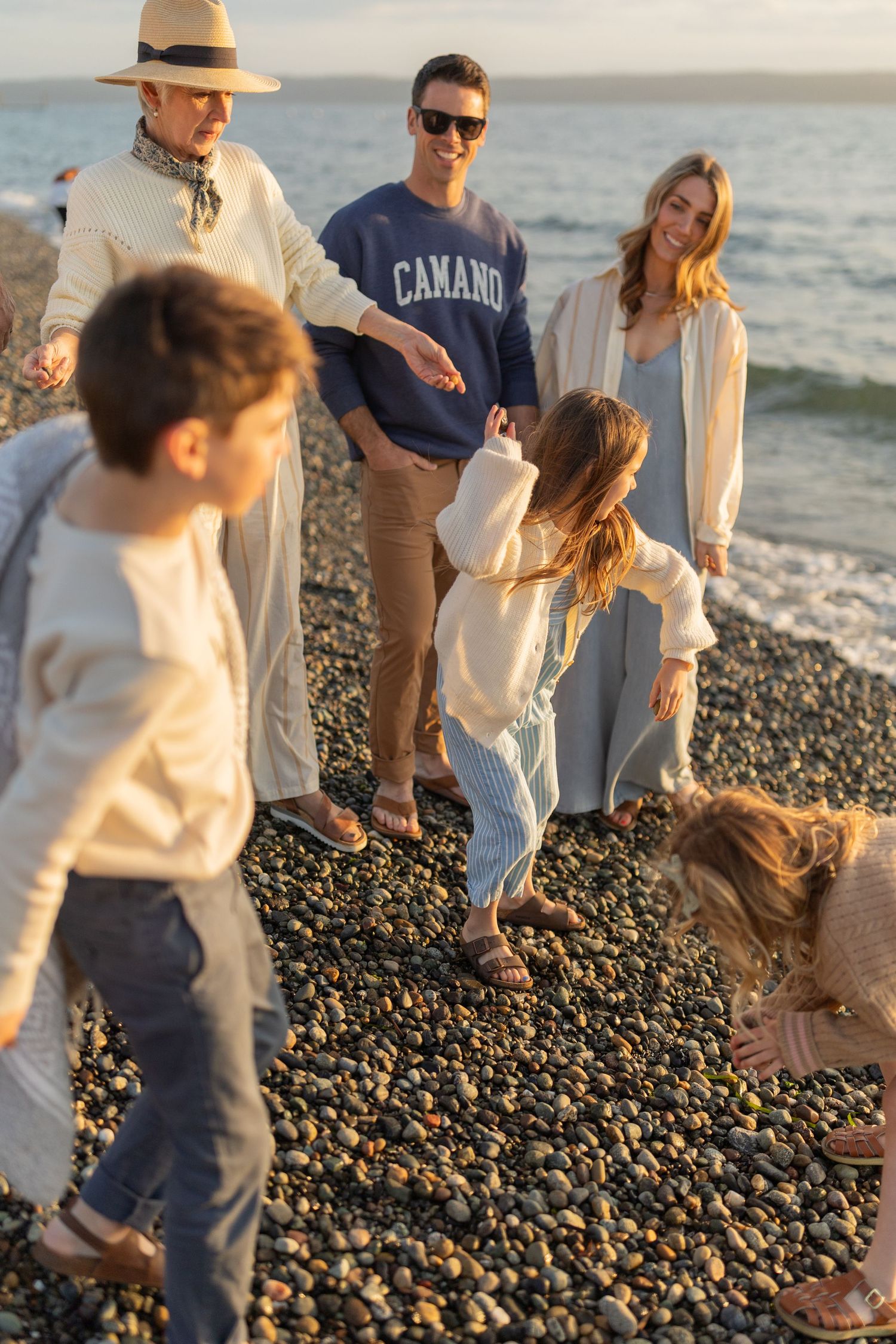 Family and dog enjoying a casual evening stroll along a rocky beach at sunset.