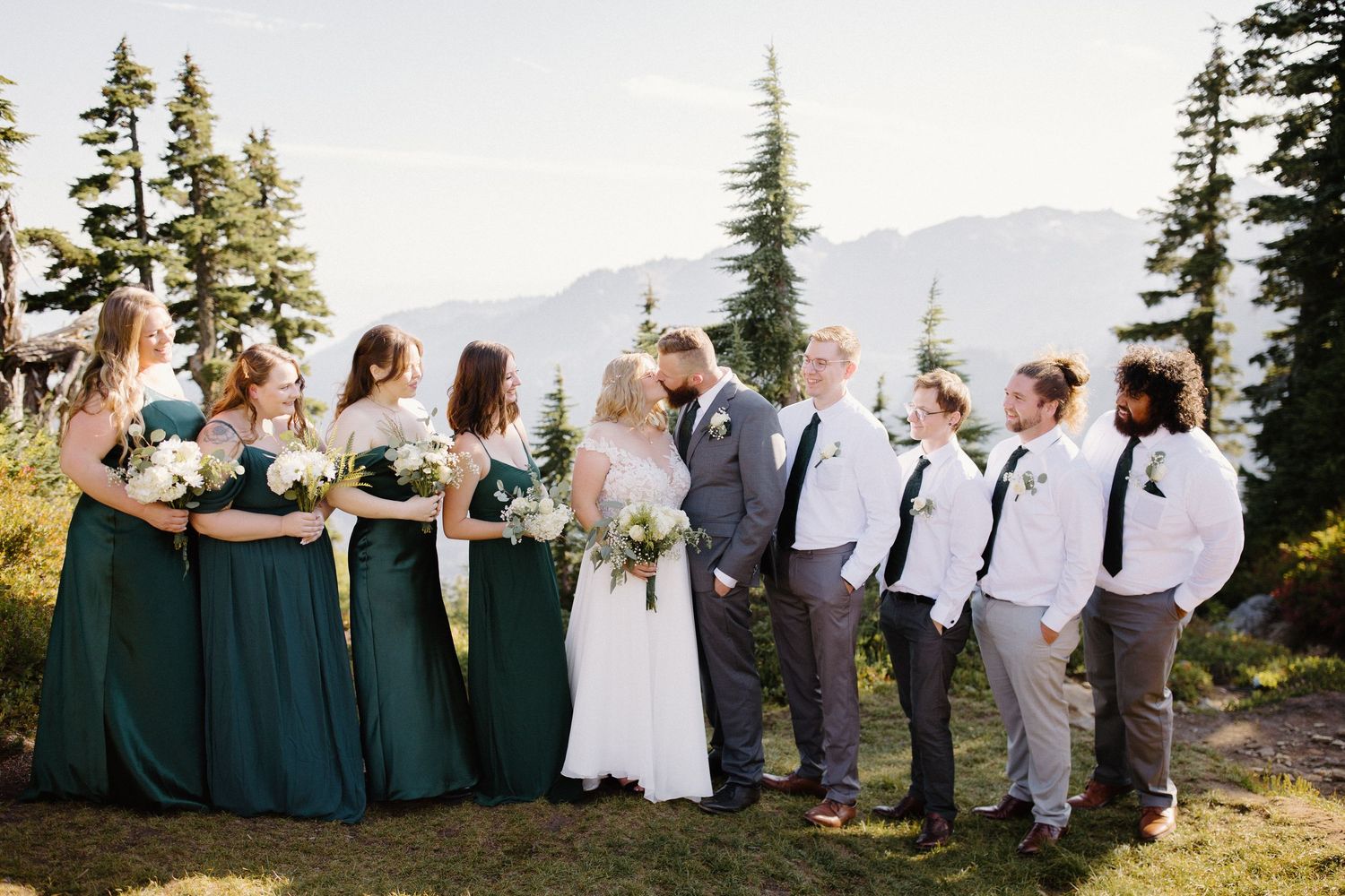 Wedding party members line up against mountain backdrop in coordinated formal attire.