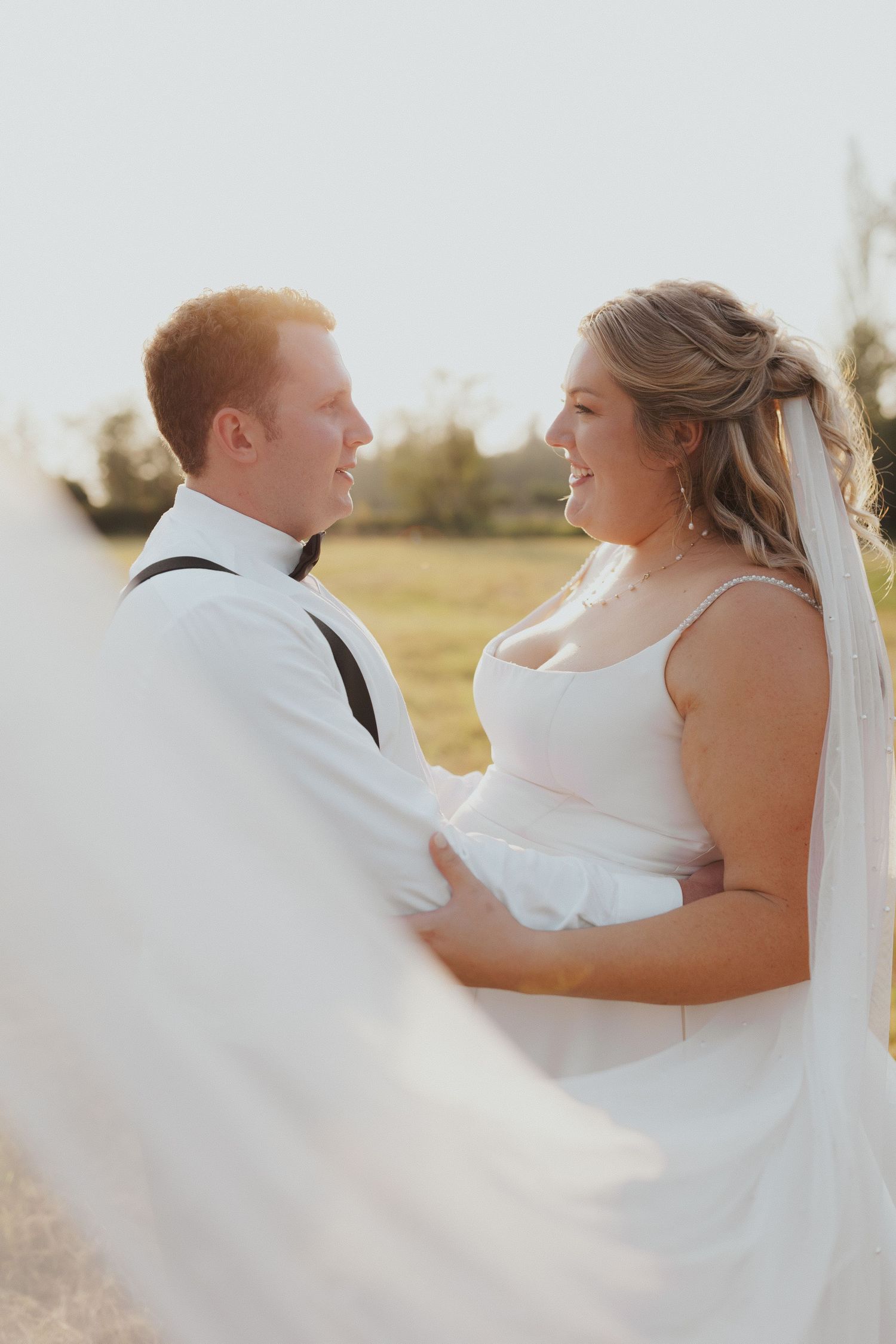 A romantic moment between newlyweds in a sun-lit field with flowing white wedding dress.