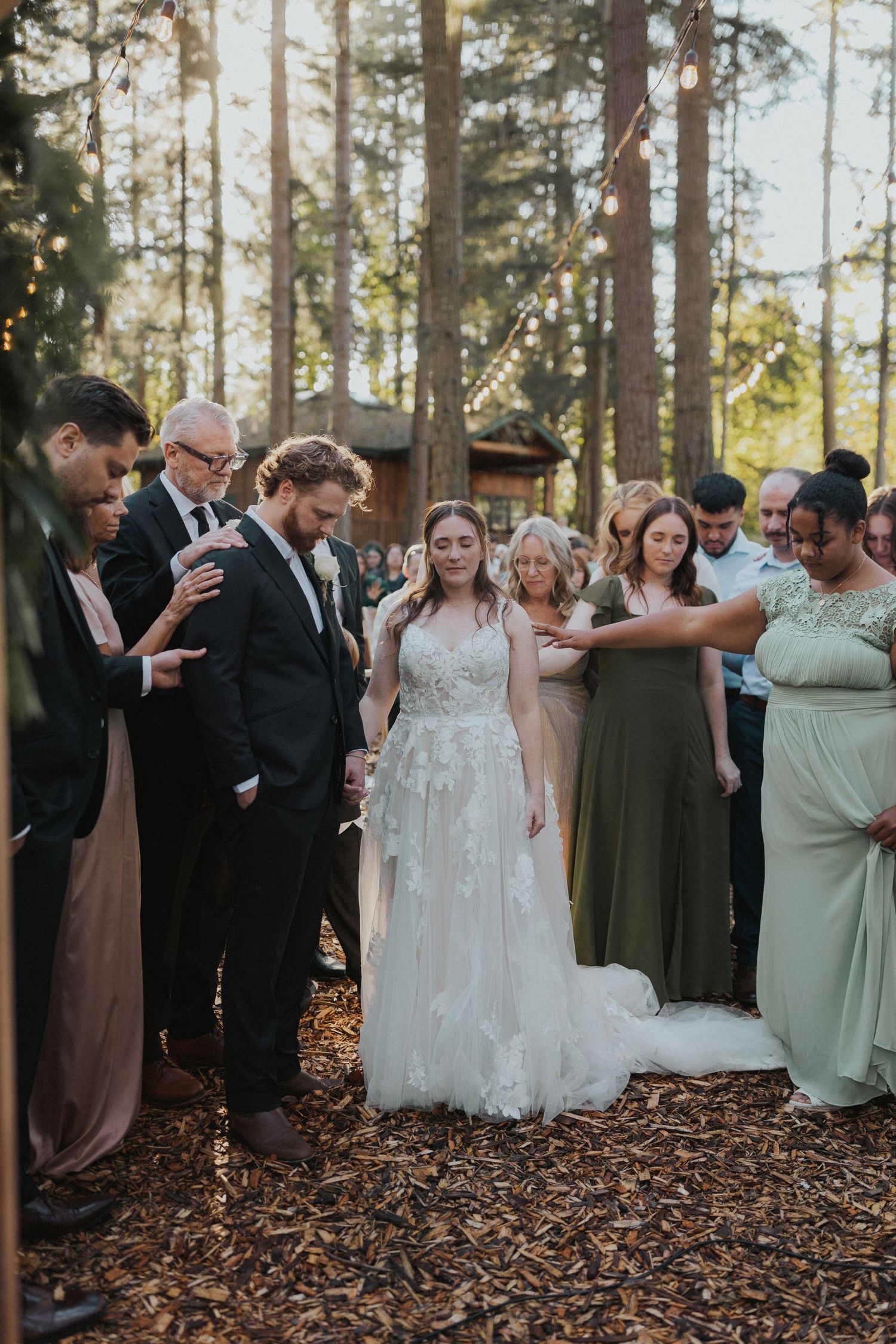 Wedding attendees stand together during a ceremony in a natural forest setting.