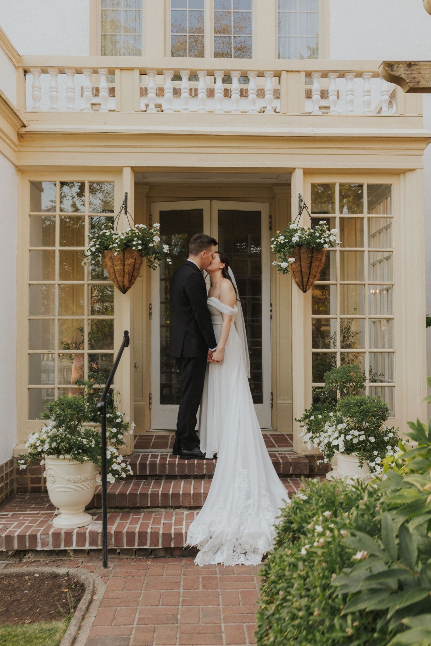 Elegant wedding dress displayed on a brick porch with white columns and lush garden landscaping.