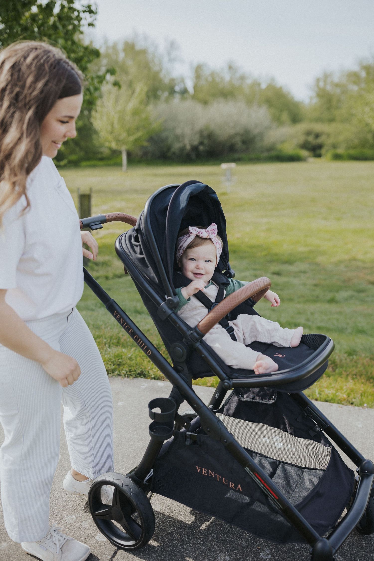 Baby stroller being pushed across green grass field on sunny day.