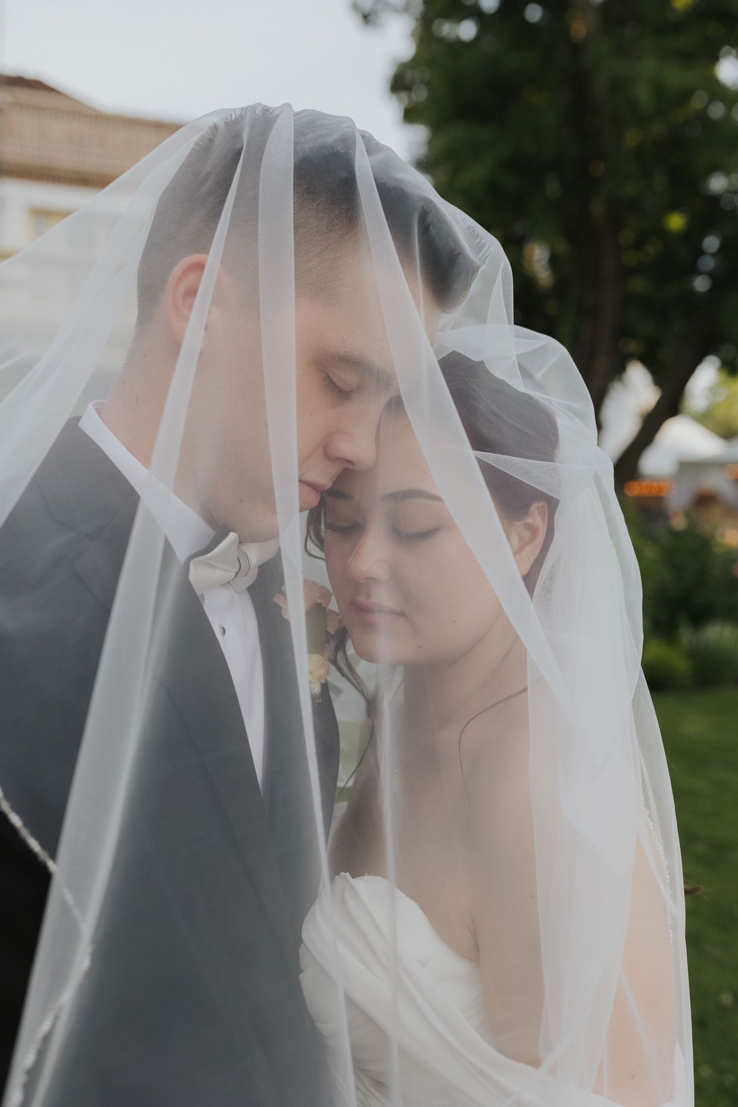 Intimate wedding portrait under a delicate white veil in an outdoor garden setting.